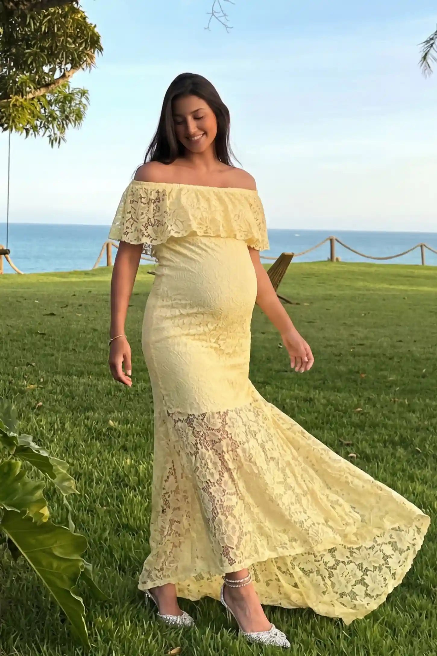 Lace Off-the-Shoulder Flutter Sleeve Maternity Maxi Dress Lace Off-the-Shoulder Flutter Sleeve Maternity Dress in Beige featuring a ruffled neckline on a front-facing pregnant model.