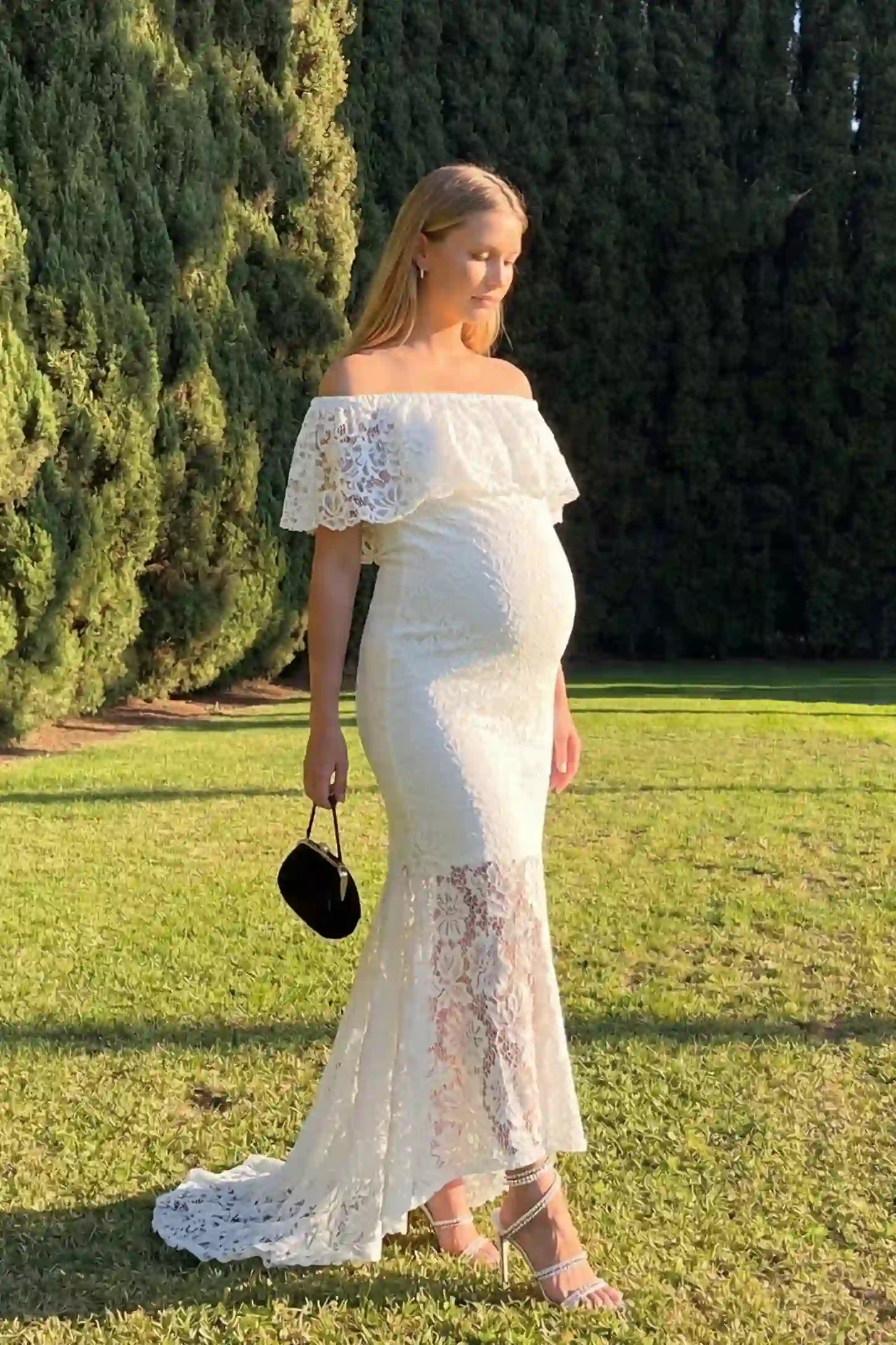 Lace Off-the-Shoulder Flutter Sleeve Maternity Maxi Dress Lace Off-the-Shoulder Flutter Sleeve Maternity Dress in White featuring a sheer lace skirt detail on a side-view pregnant model.