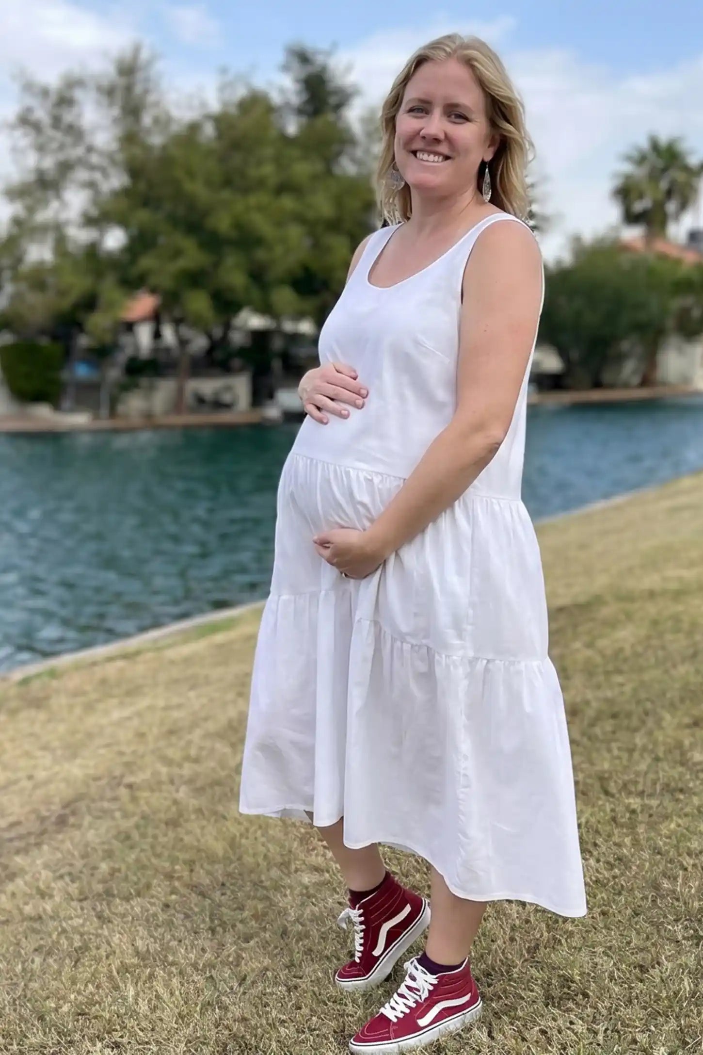 Layered Skirt A-Line Maternity Midi Dress Layered skirt A-line maternity midi dress in white with sleeveless design, side view on pregnant model
