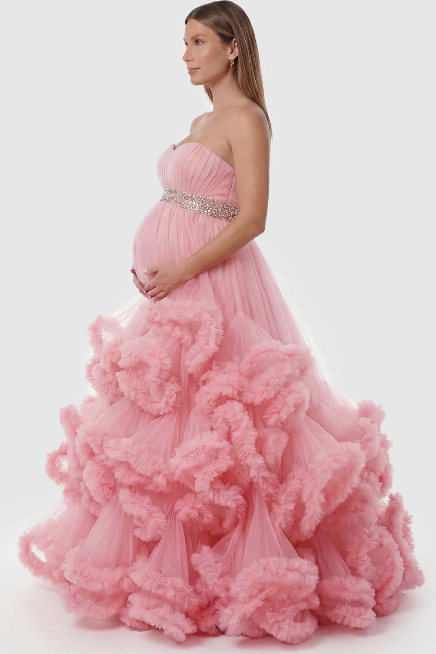 Multi-Layered Pleated Tulle Strapless Bodice Maxi Maternity Gown Multi-layered pleated tulle strapless bodice maxi maternity gown in pink featuring layered pleated tulle skirt in side view on a pregnant model