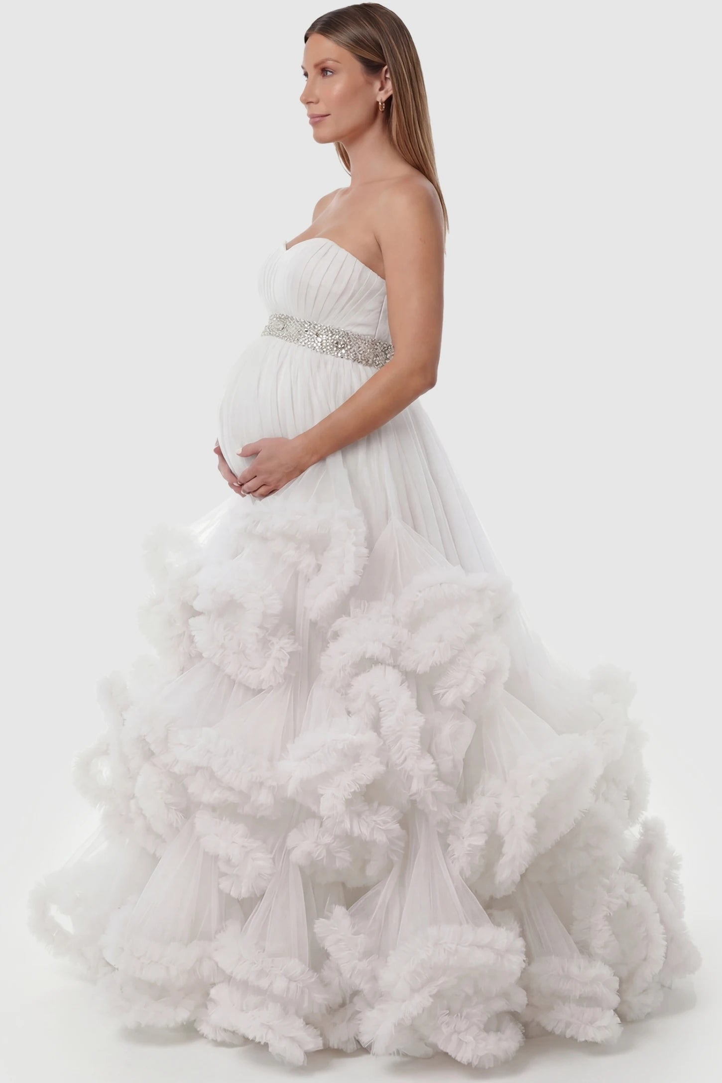 Multi-Layered Pleated Tulle Strapless Bodice Maxi Maternity Gown Multi-layered pleated tulle strapless bodice maxi maternity gown in white featuring layered pleated tulle skirt in side view on a pregnant model