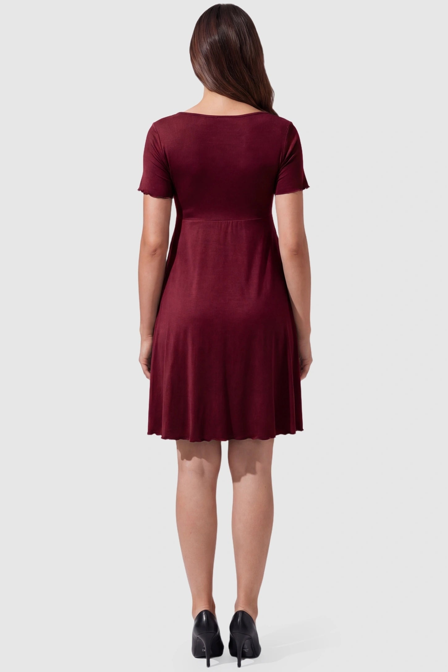 Lettuce Trim A-Line Mini Maternity Dress Lettuce Trim A-Line Mini Maternity Dress in Burgundy featuring an empire waistline on the back of a pregnant model.
