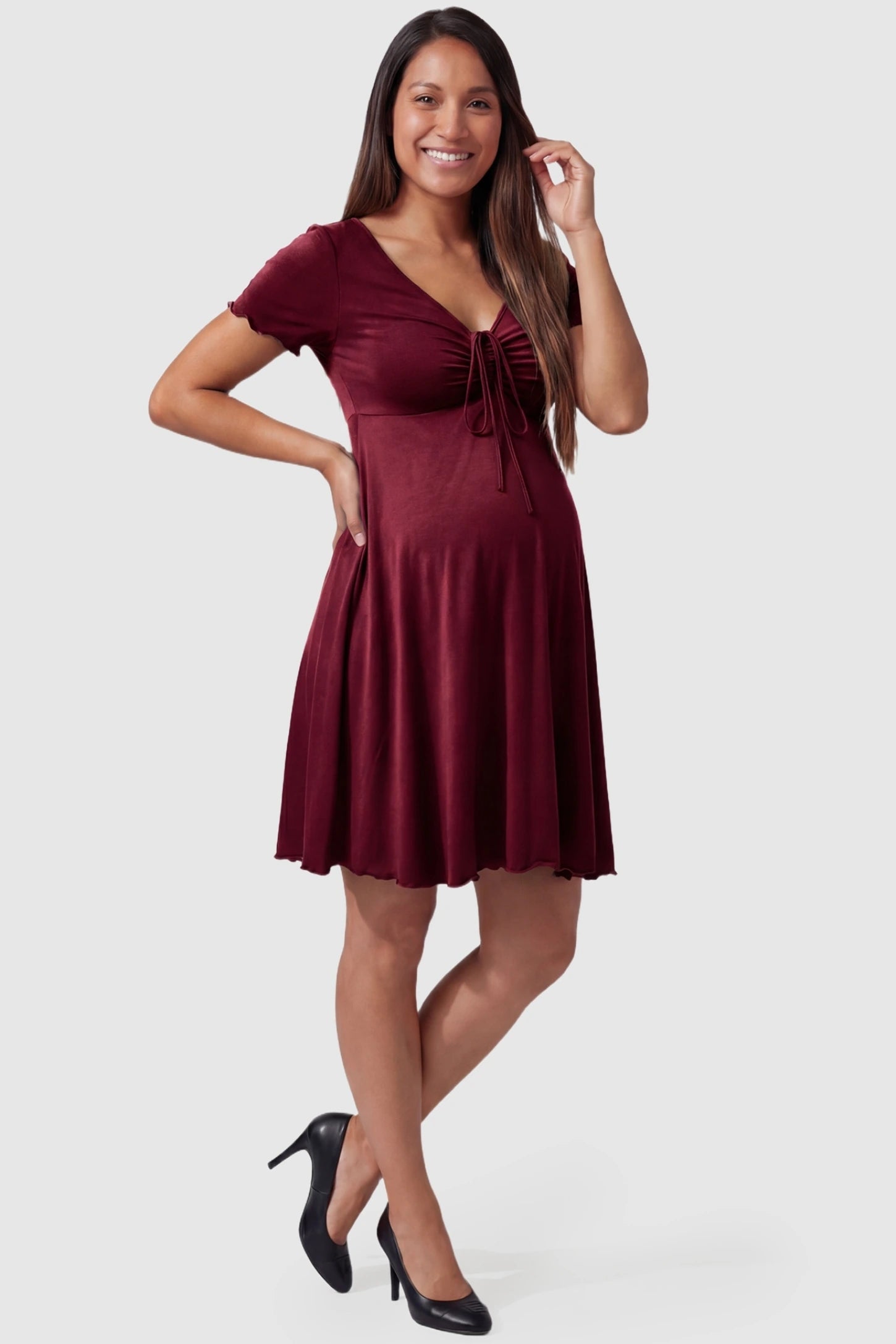 Lettuce Trim A-Line Mini Maternity Dress in Burgundy featuring a knot front drawstring on a pregnant model.