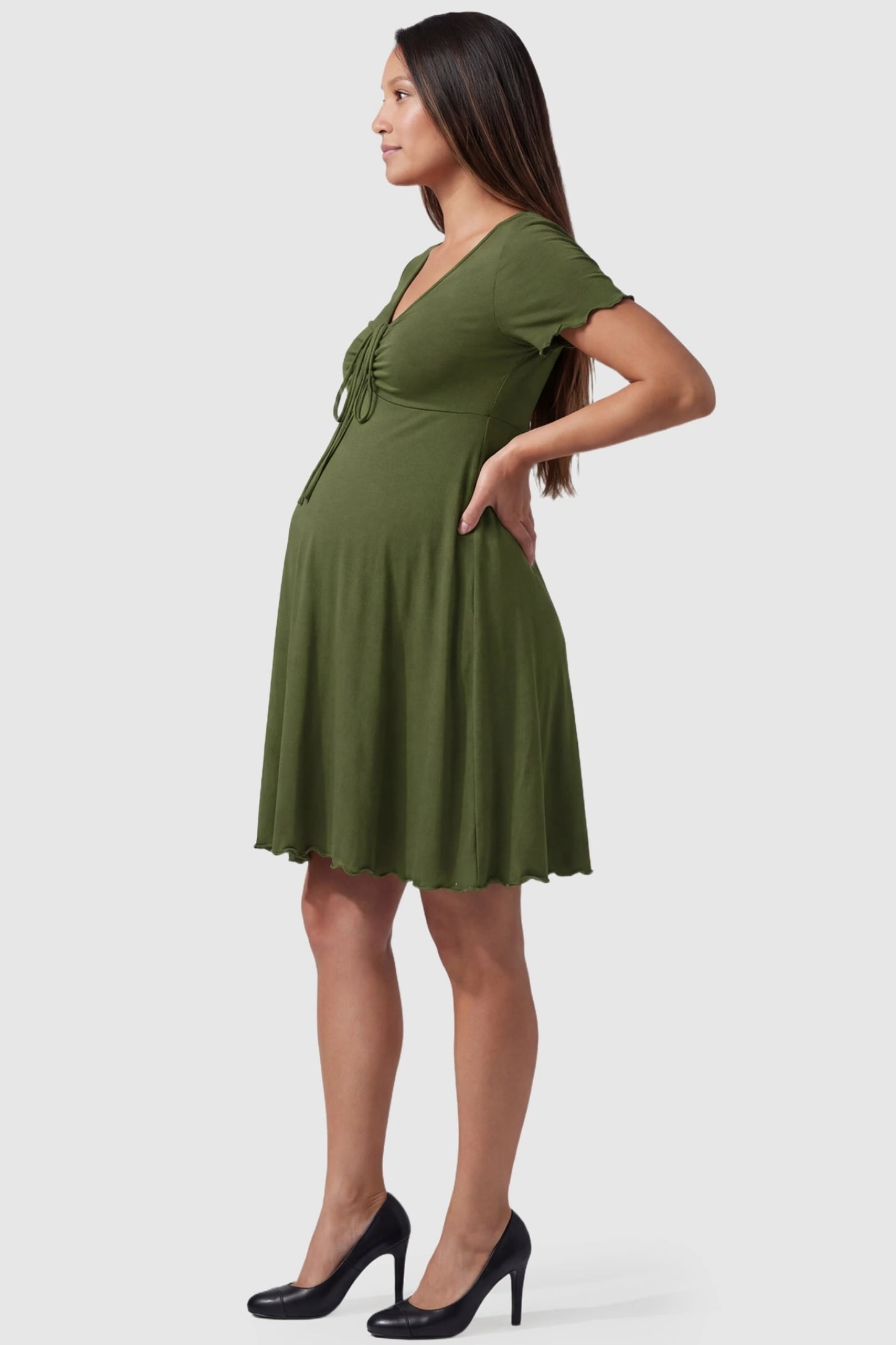 Lettuce Trim A-Line Mini Maternity Dress Lettuce Trim A-Line Mini Maternity Dress in Green featuring a curve-hugging silhouette on the side profile of a pregnant model.