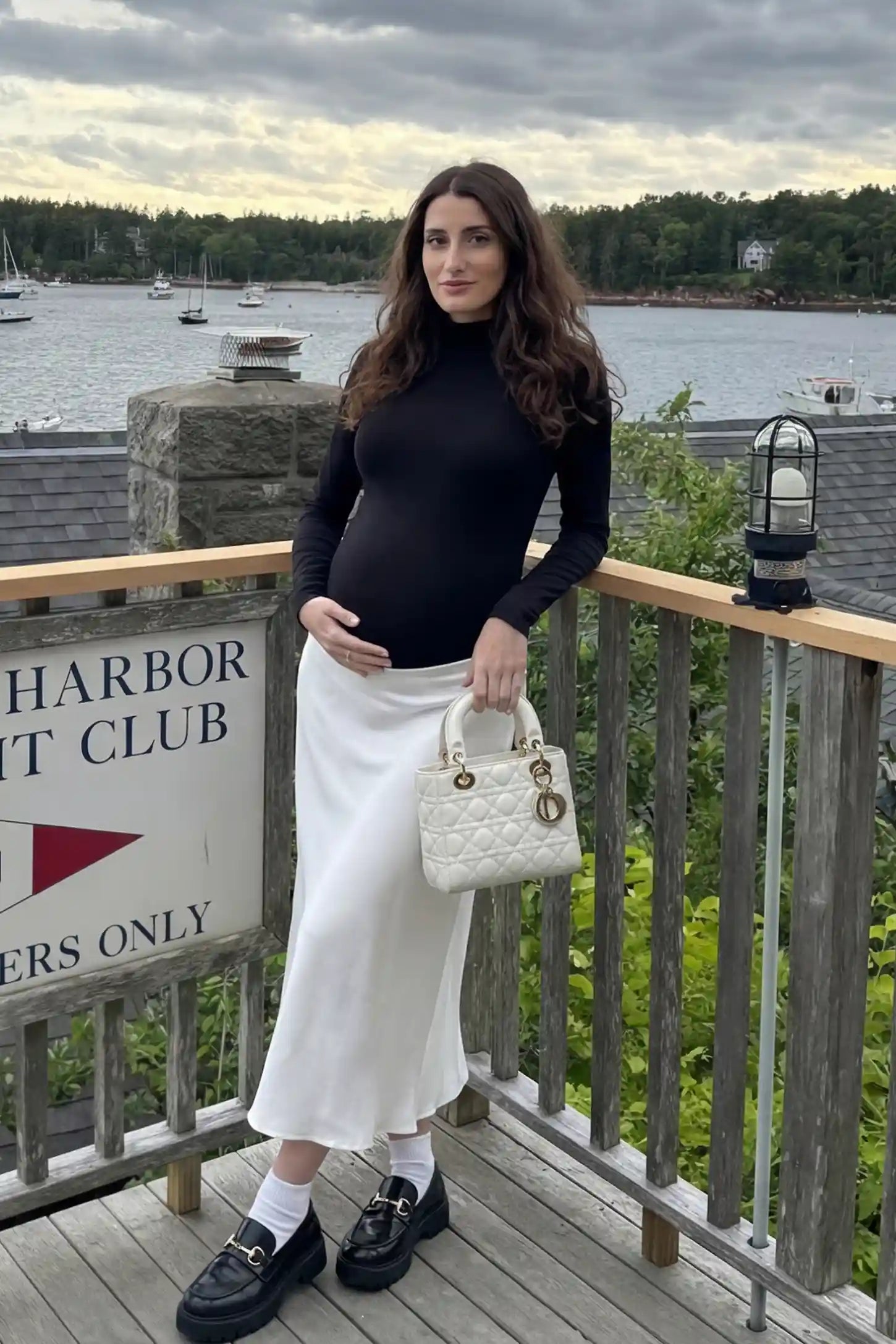 Mock-Neck Long-Sleeve Maternity Bodysuit Mock-neck long-sleeve maternity bodysuit in black with long sleeves & paired with skirt, on front view pregnant model