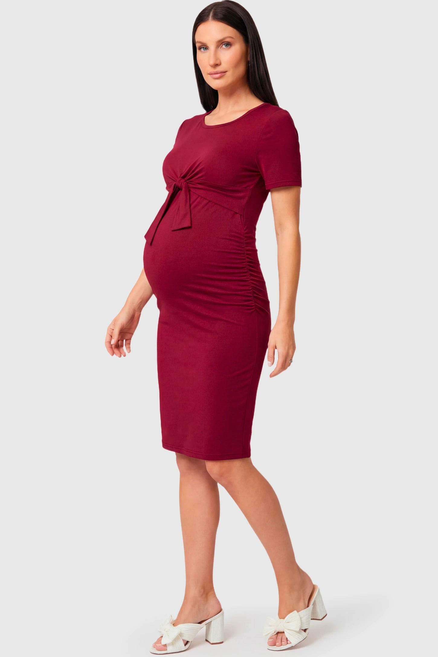 Crew Neck Bodycon Maternity & Nursing Midi Dress in wine red featuring twist-front detail and short sleeves on a  pregnant model.