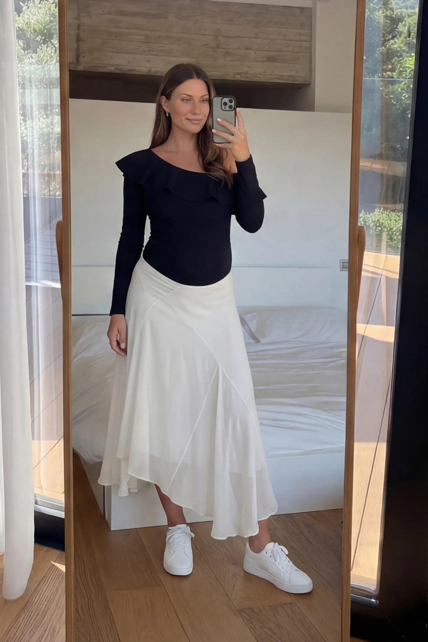 Off-Shoulder Ruffle Trim Maternity Bodysuit Off-shoulder ruffle trim maternity bodysuit in black with long-sleeve and paired with skirt, front view on pregnant model