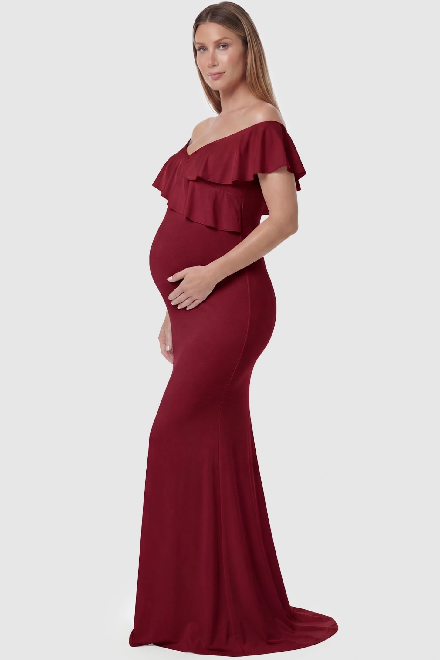 Ruffle Off-Shoulder Slim Fit Maxi Maternity Dress Ruffle off-shoulder slim fit maxi maternity dress in wine red featuring off-shoulder and elegant ruffle detailing fabric in side view on a pregnant model