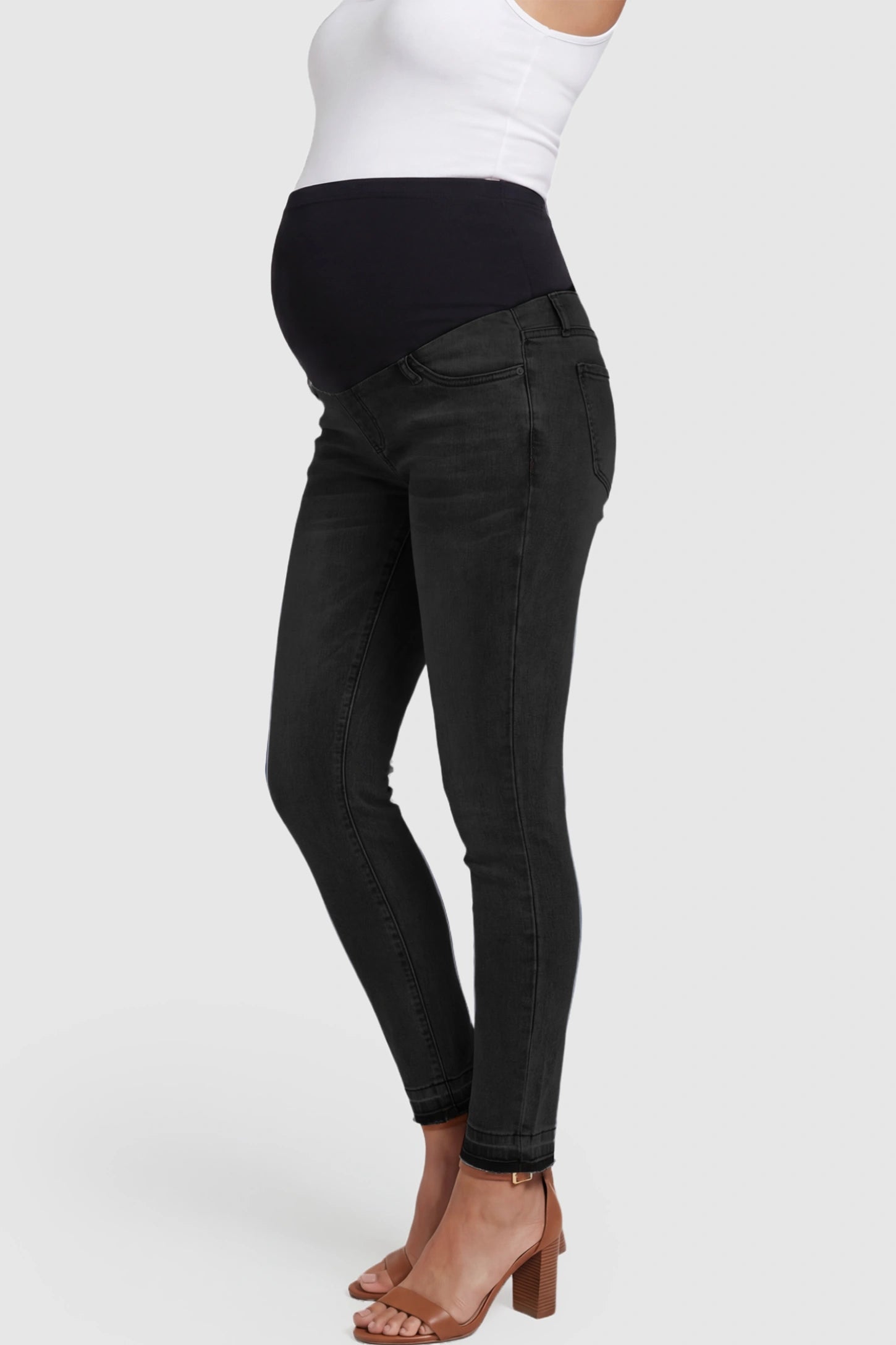 Full Panel Released Hem Maternity Skinny Jeans Full Panel Released Hem Maternity Skinny Jeans in Black featuring a released hem and over-the-belly panel on a pregnant model showing side.
