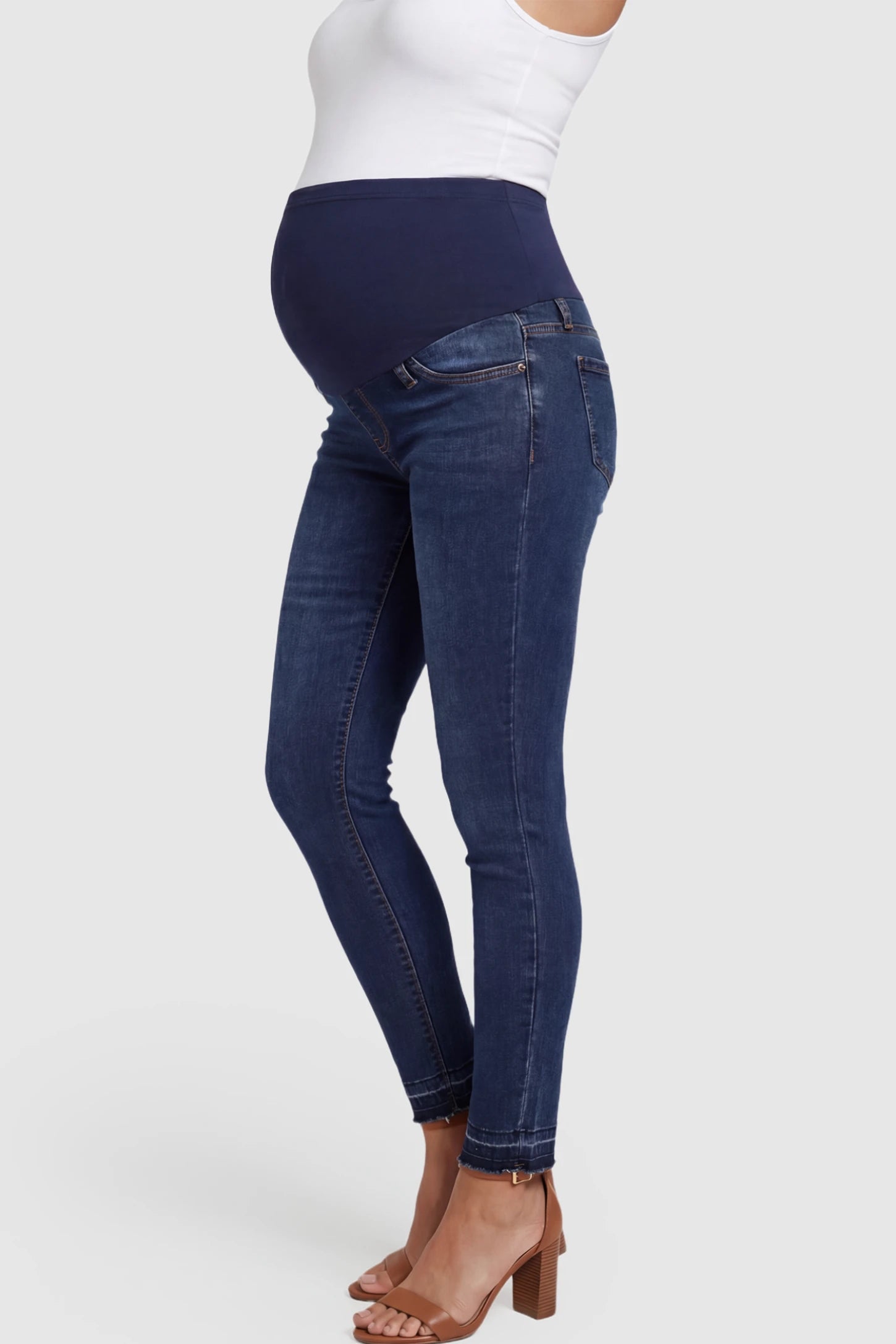 Full Panel Released Hem Maternity Skinny Jeans Full Panel Released Hem Maternity Skinny Jeans in Dark Blue featuring a released hem and over-the-belly panel on a pregnant model showing side.