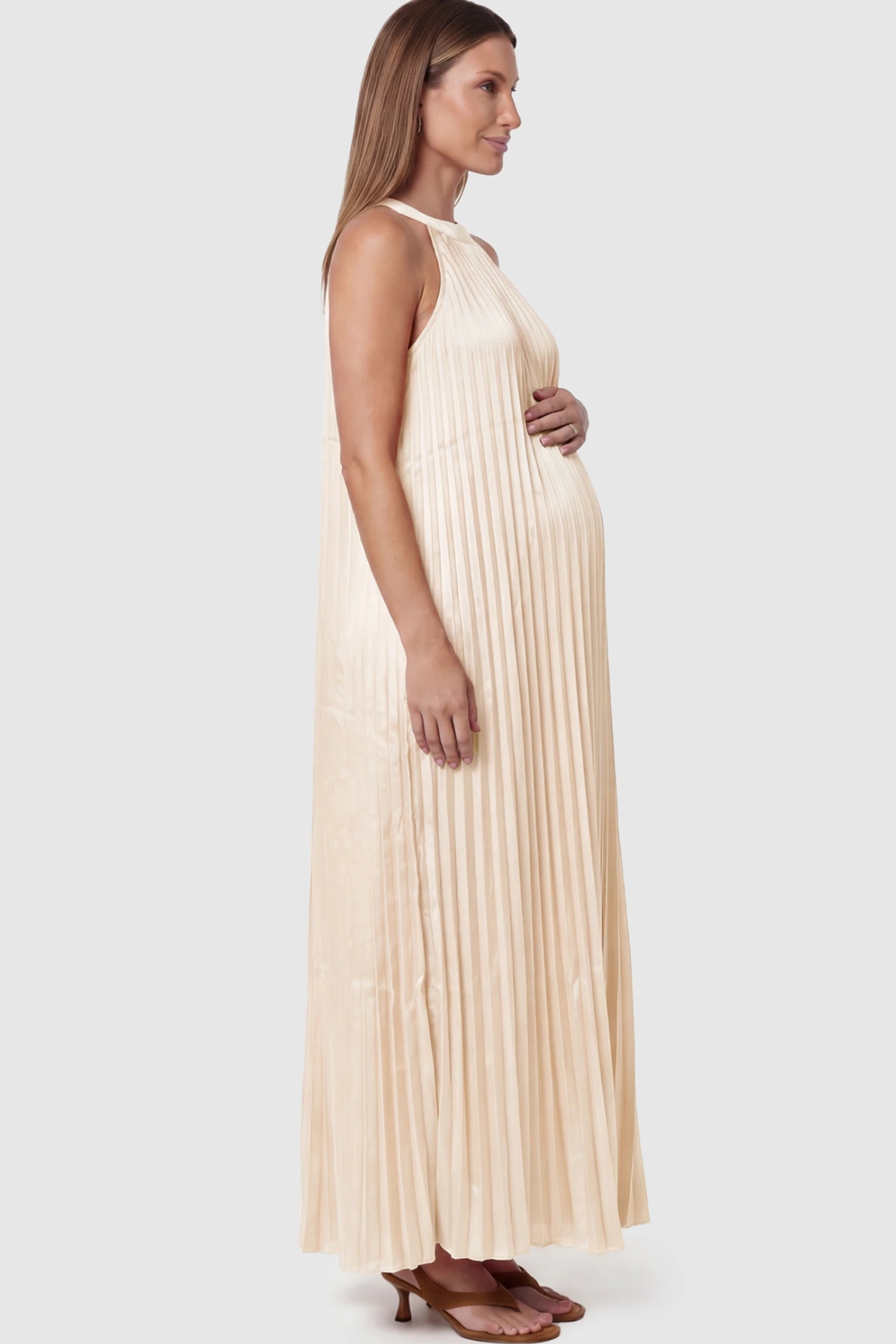 Pleated Faux Silk Halter Maternity Maxi Dress Pleated Faux Silk Halter Maternity Maxi Dress in Champagne featuring micro-pleat texture on a pregnant model facing left.