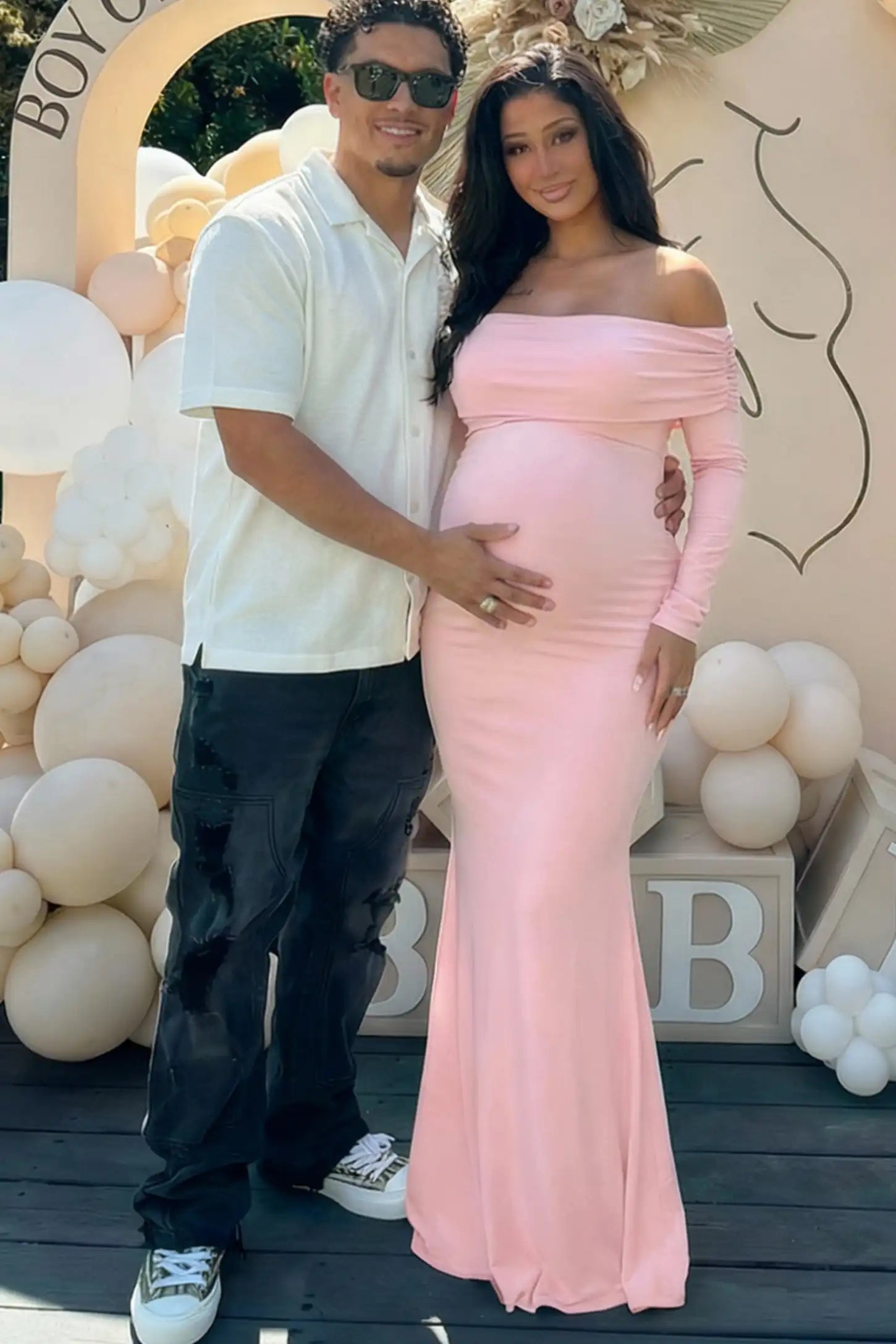 Solid Off Shoulder Bodycon Maternity Maxi Dress Off Shoulder Bodycon Maternity Maxi Dress in Pink featuring a smooth stretch finish on a pregnant model posing with a partner.