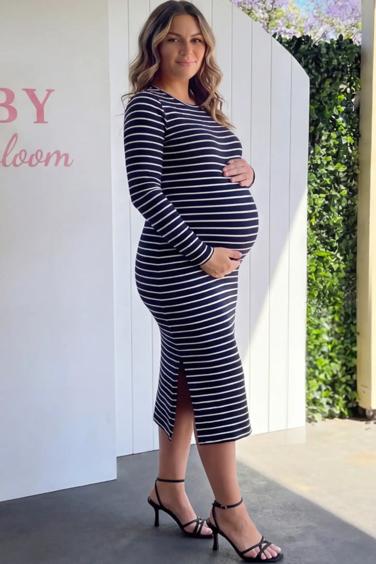 Striped side slit long sleeve bodycon maternity midi dress in black and white featuring a bump-flattering fit on a pregnant model.