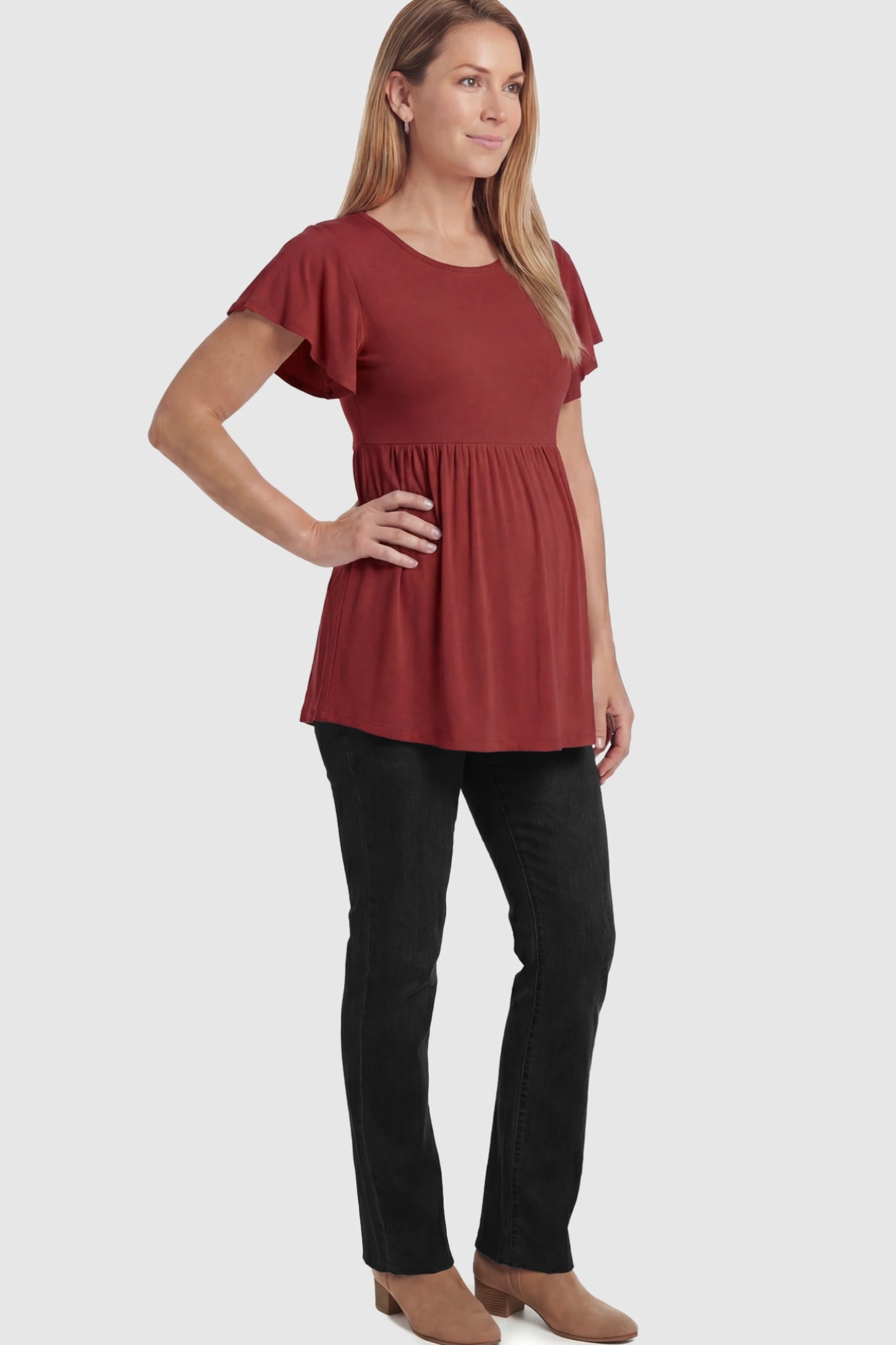 Solid Ruffled-Sleeve Flowy Maternity Top Solid Ruffled-Sleeve Flowy Maternity Top in Red featuring a pleated empire waist paired with black jeans and boots on a pregnant model in  a full body image.