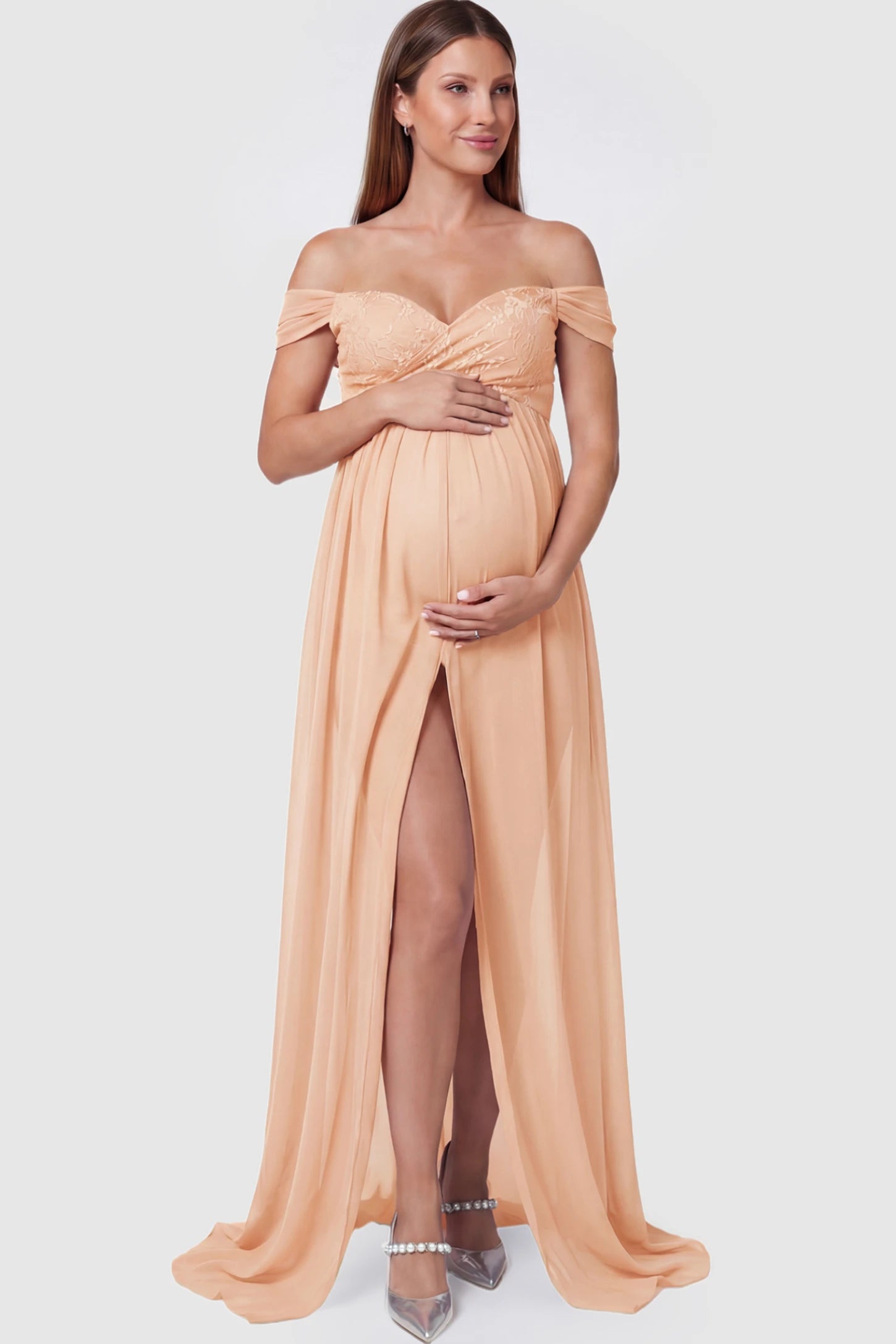 Lace Off Shoulder Slit Front Maternity Photoshoot Gown Lace Off Shoulder Slit Front Maternity Photoshoot Gown in light peach featuring a flowy chiffon opening on a pregnant model.