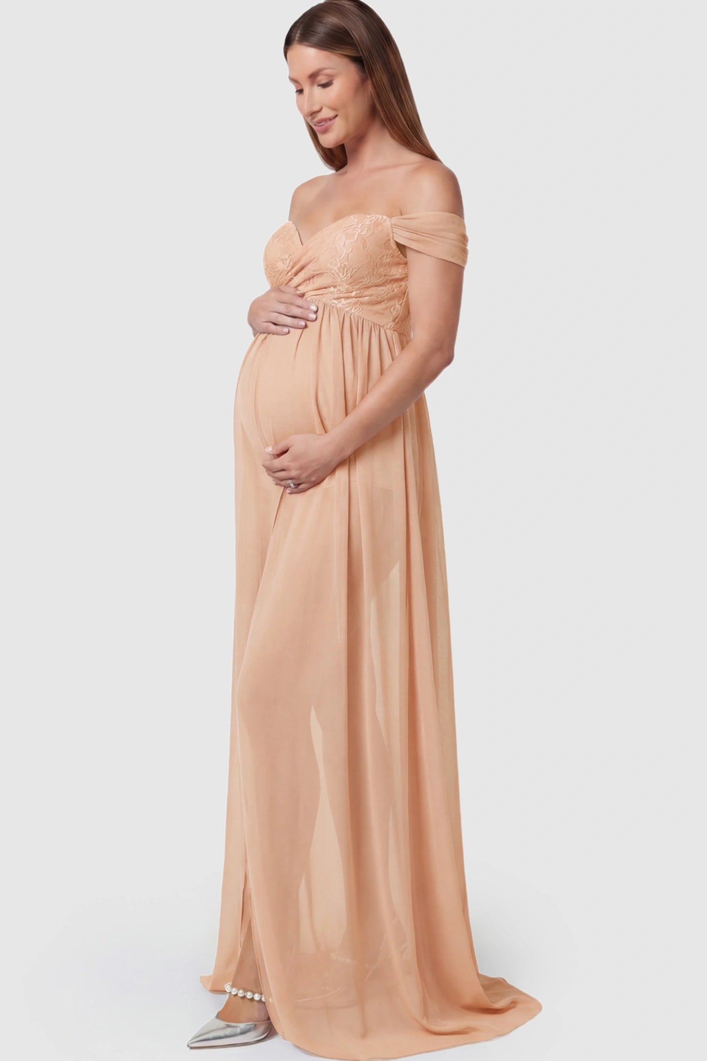 Lace Off Shoulder Slit Front Maternity Photoshoot Gown Lace Off Shoulder Slit Front Maternity Photoshoot Gown in light peach featuring a flowy chiffon opening on a pregnant model.