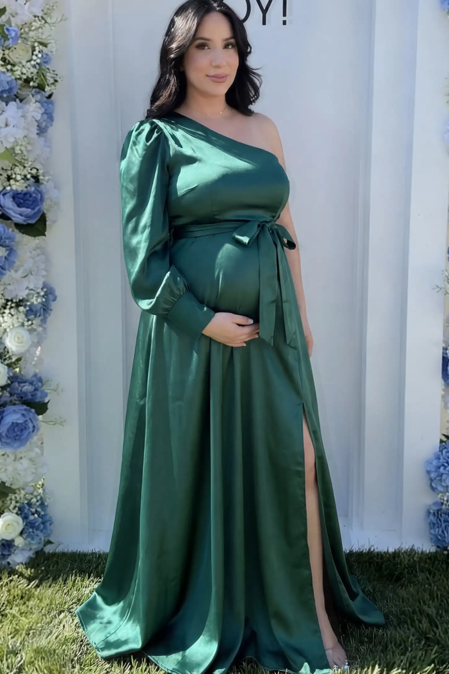 Satin One Shoulder Belted Maternity Maxi Dress Satin One-Shoulder Belted Maternity Maxi Dress in Green featuring a side slit and waist tie on a pregnant model.
