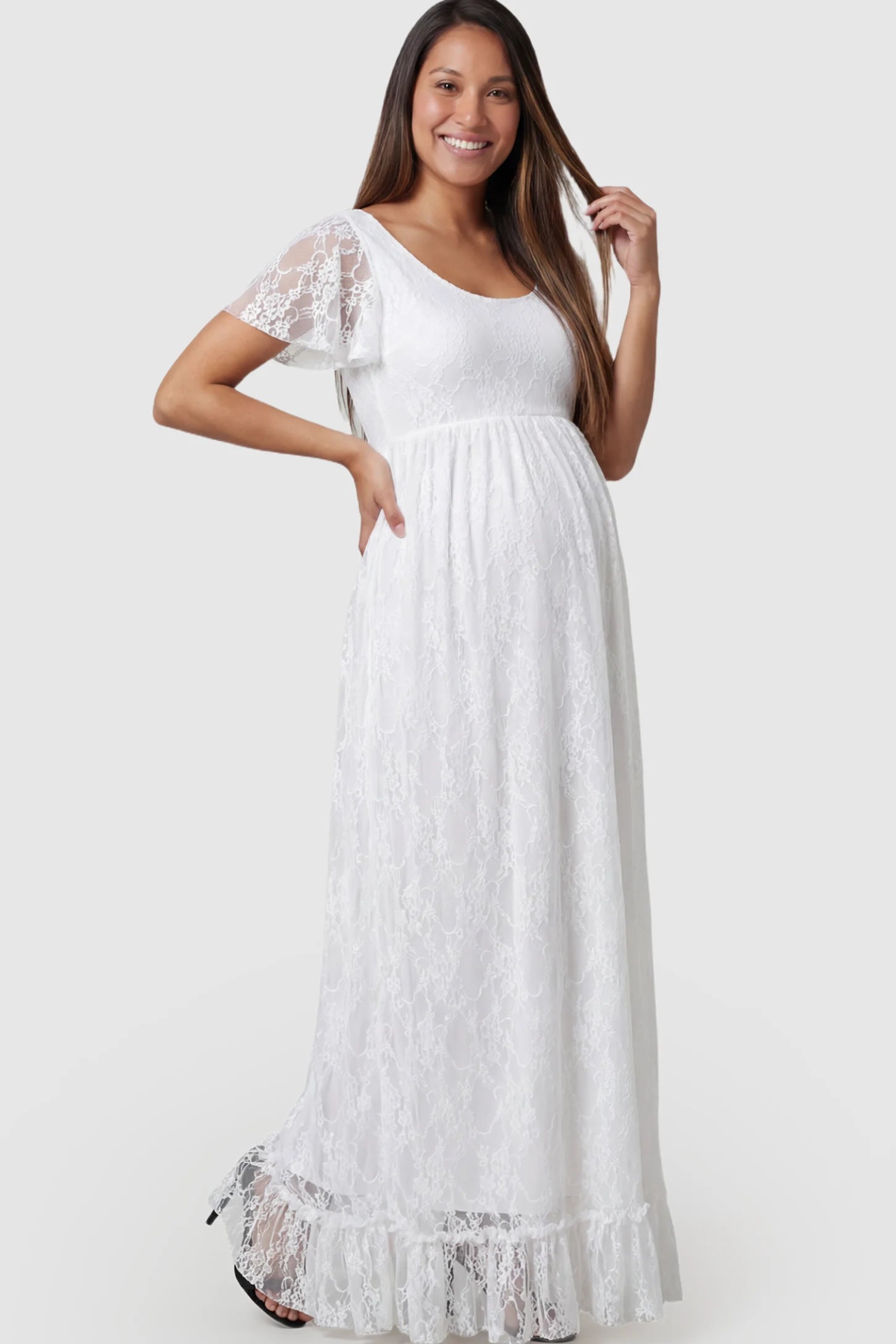 Floral Lace Flutter Sleeve Maternity Maxi Dress Floral Lace Flutter Sleeve Maxi Maternity Dress in White featuring delicate lace and an empire waist on a pregnant model.
