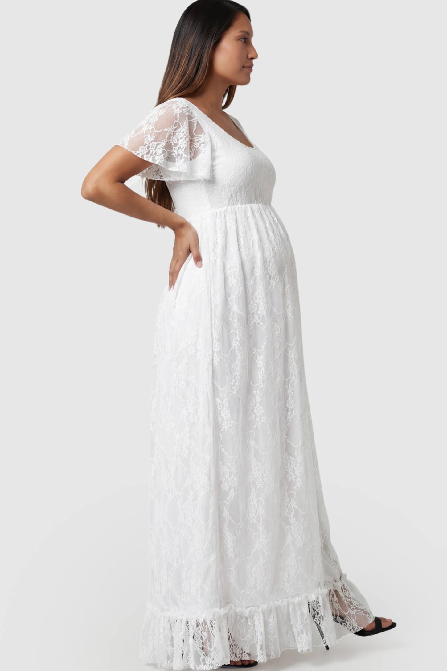 Floral Lace Flutter Sleeve Maternity Maxi Dress Floral Lace Flutter Sleeve Maxi Maternity Dress in White featuring delicate lace and an empire waist on a pregnant model.