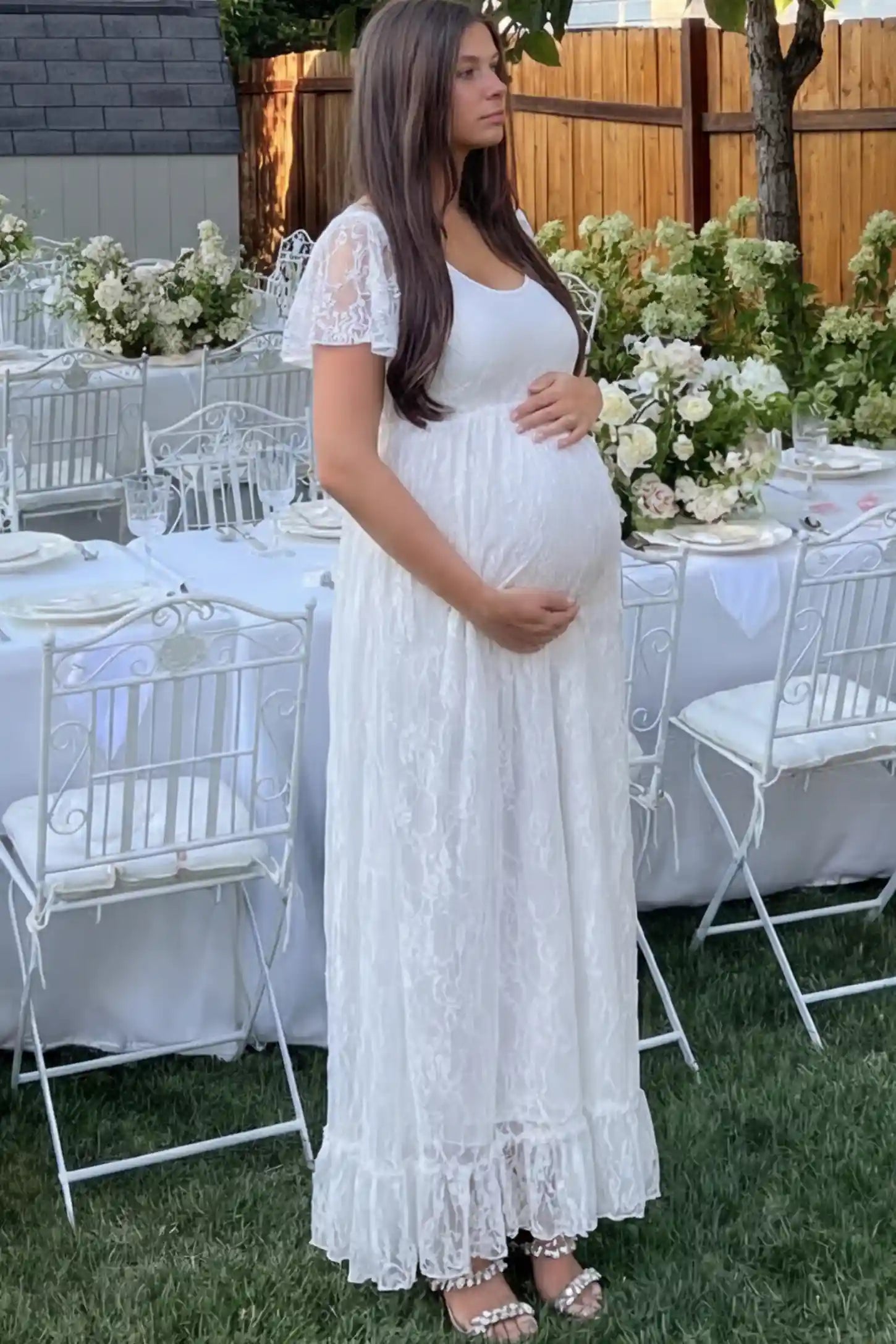 Floral Lace Flutter Sleeve Maternity Maxi Dress Floral Lace Flutter Sleeve Maxi Maternity Dress in White featuring delicate lace and an empire waist on a pregnant model.