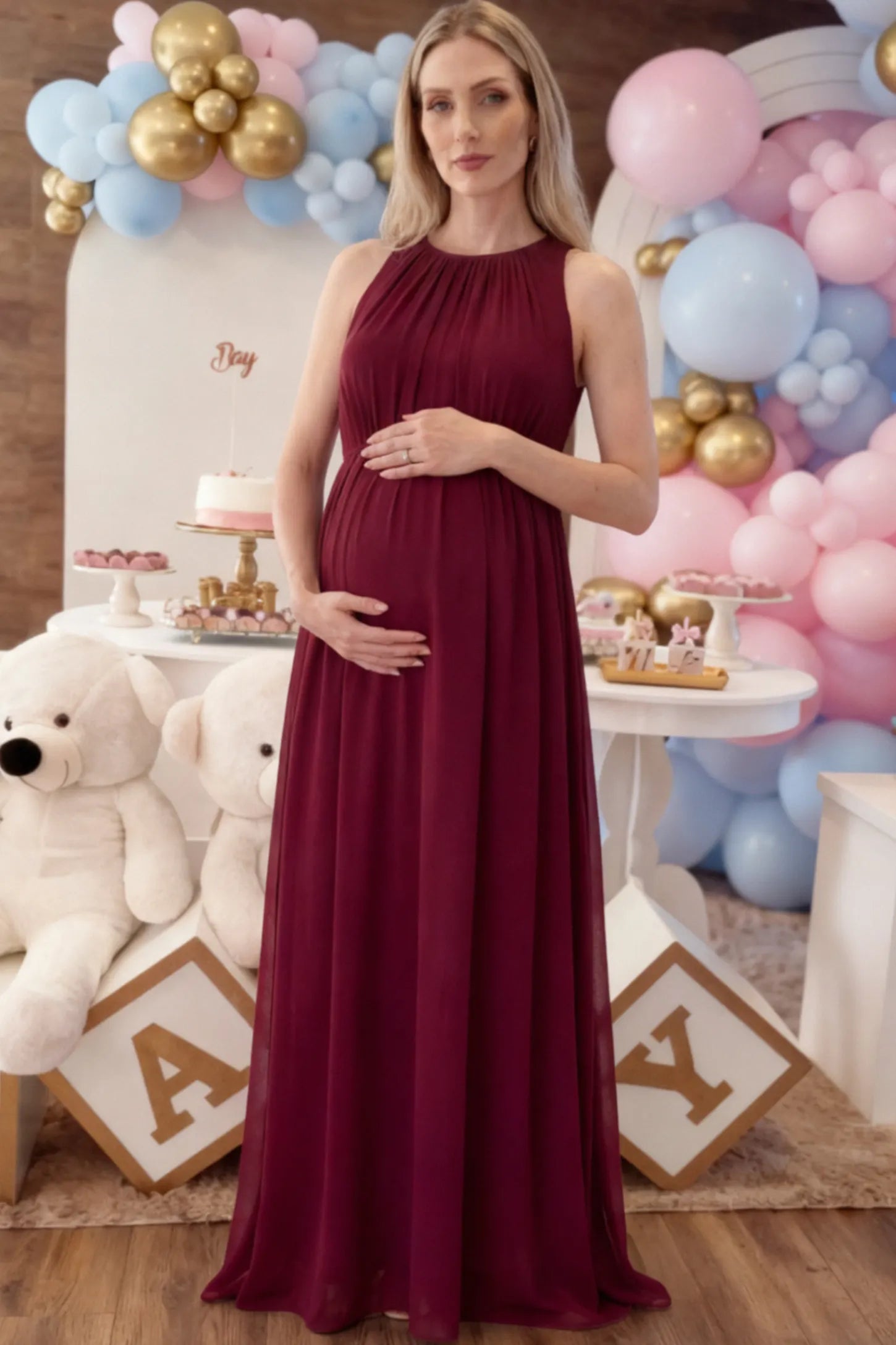 Pleated Mesh Sleeveless Maternity Maxi Dress in burgundy with an empire waist on a pregnant model.