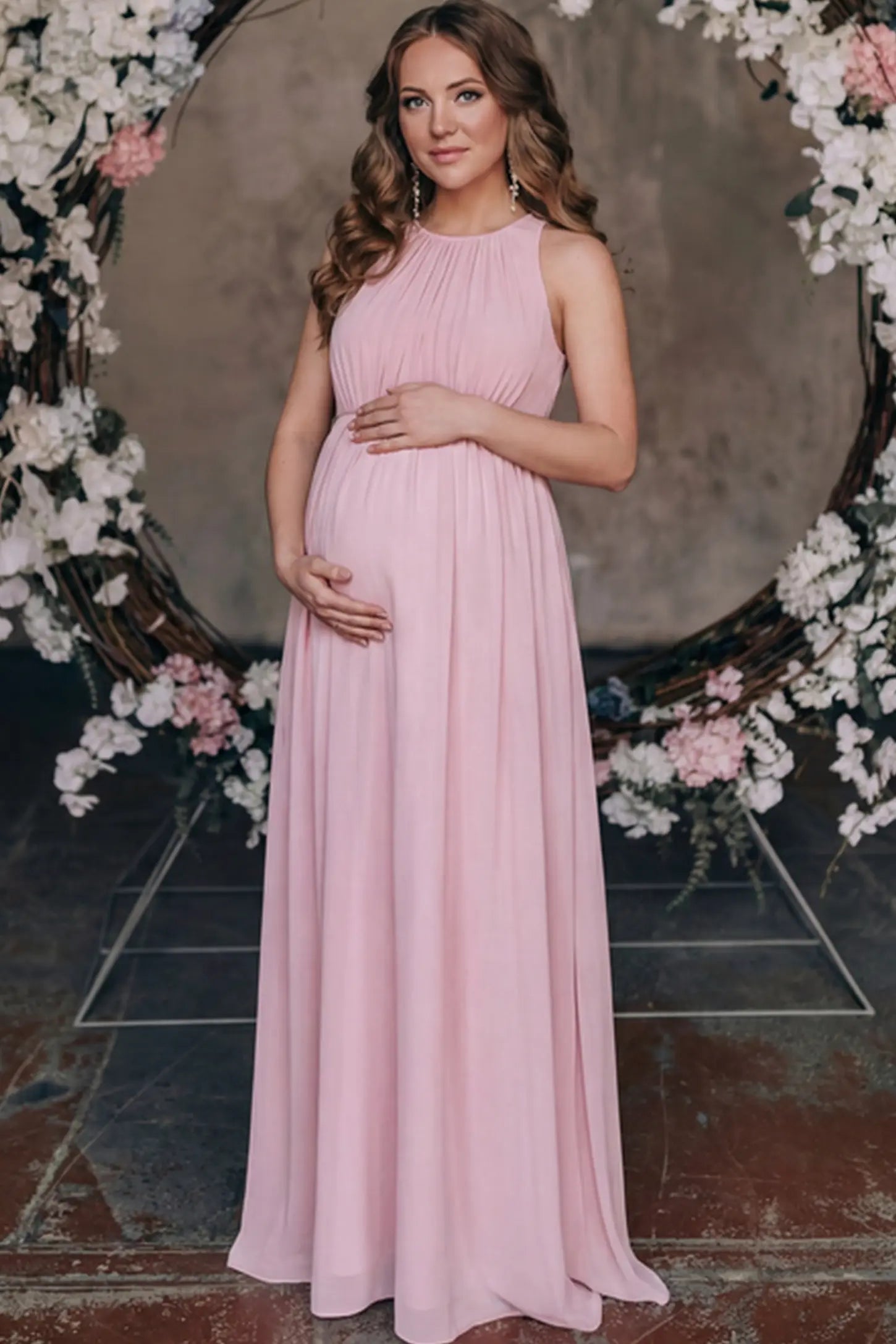 Pleated Mesh Sleeveless Maternity Photoshoot Dress Pleated Mesh Sleeveless Maternity Maxi Dress in pink with an empire waist on a pregnant model.
