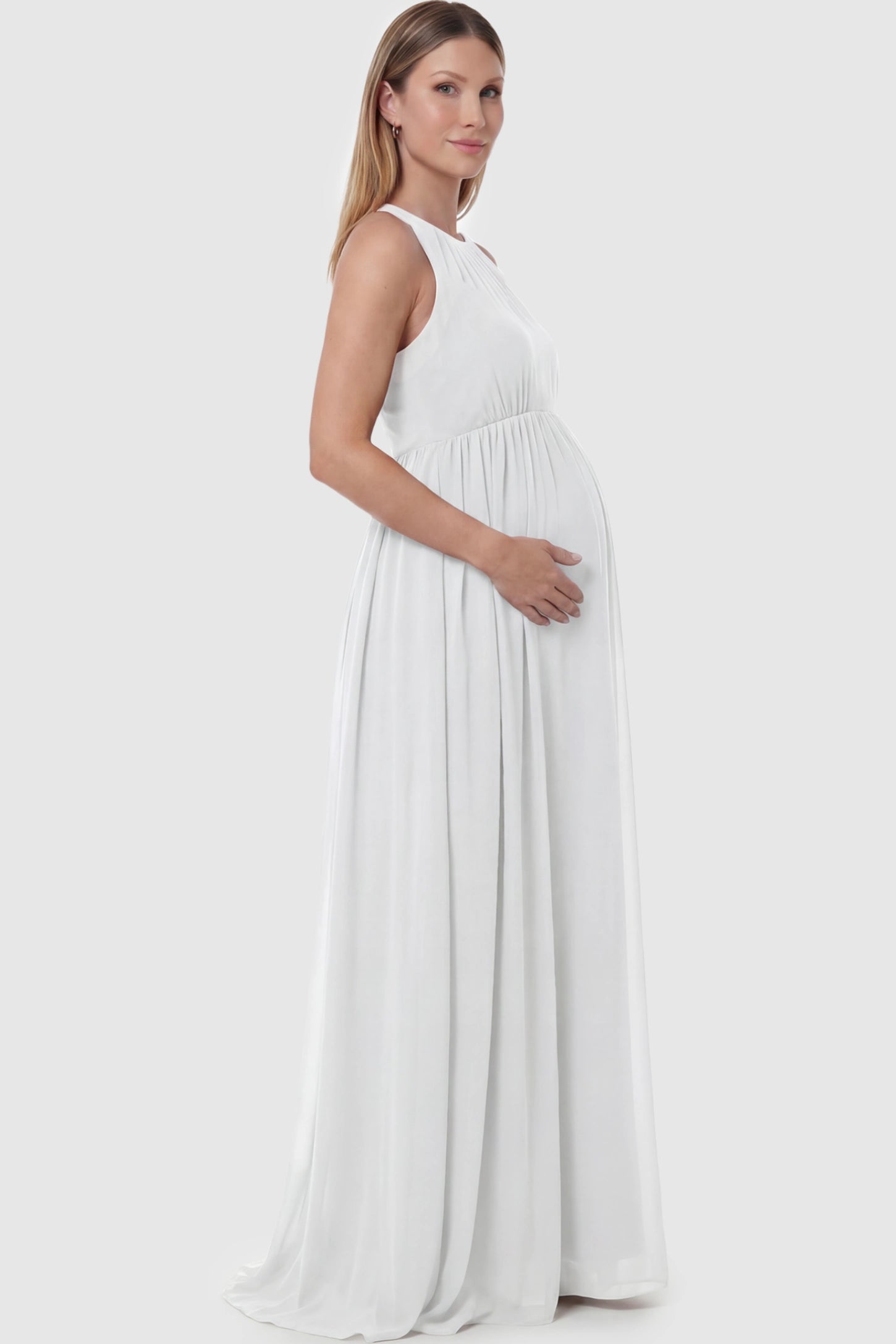 Pleated Mesh Sleeveless Maternity Photoshoot Dress Pleated Mesh Sleeveless Maternity Maxi Dress in white with an empire waist on a pregnant model.