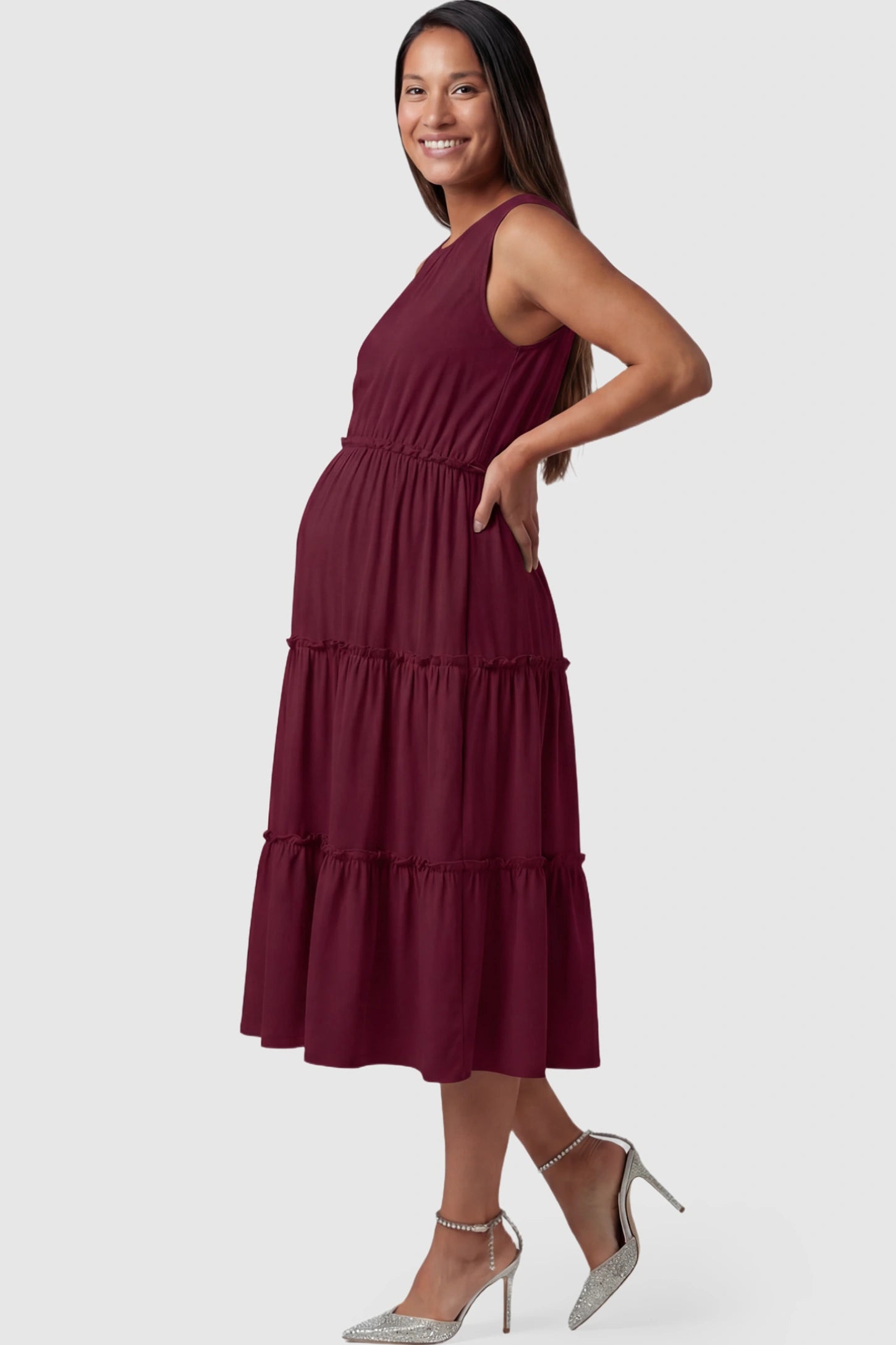 Solid Sleeveless Ruffle Tiered Maternity Midi Dress Solid Sleeveless Ruffle Tiered Maternity Midi Dress in wine red featuring a ruffle tiered skirt on a pregnant model.