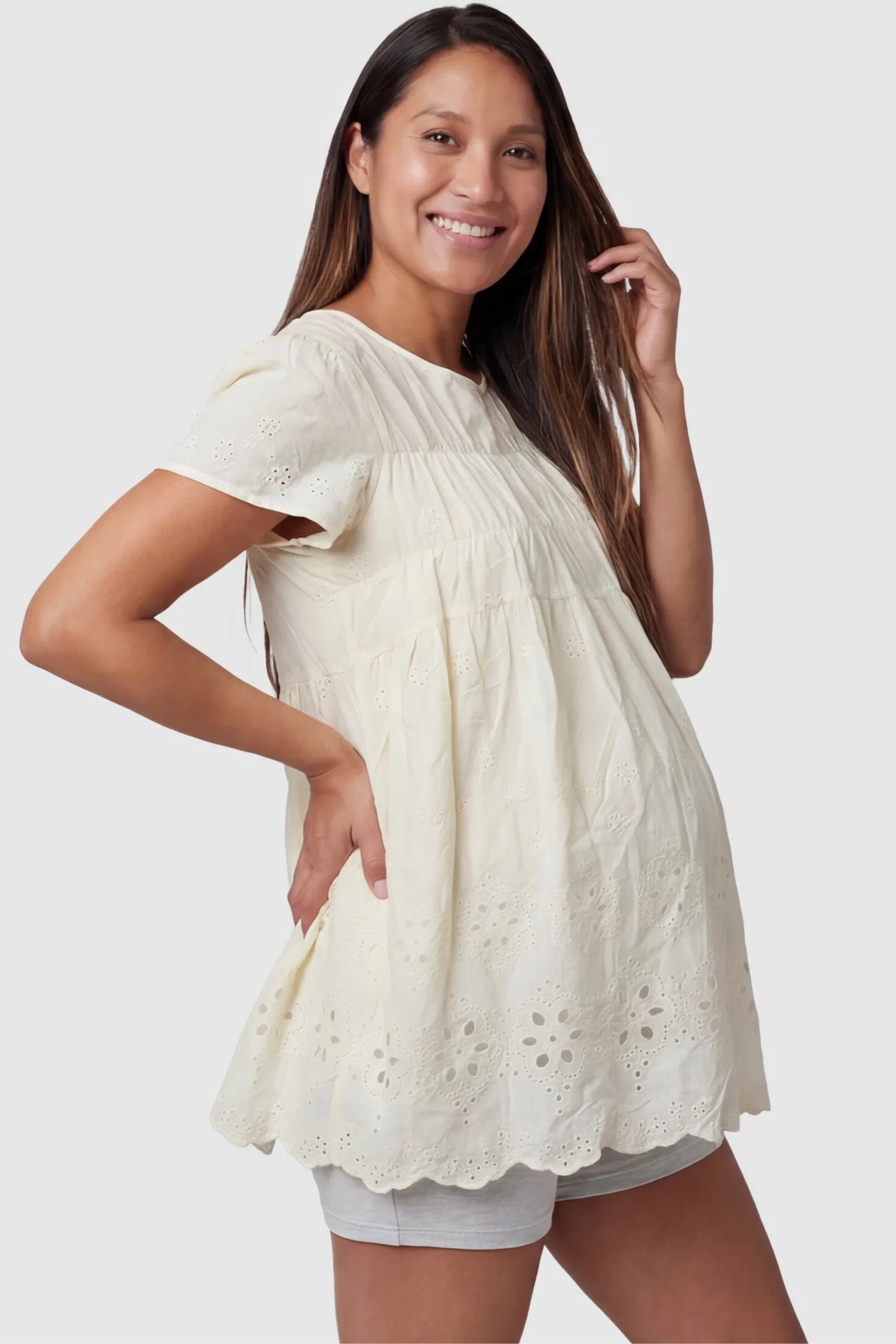 Floral eyelet round neck peplum maternity top in pale yellow with delicate floral eyelet detail, side view on pregnant model