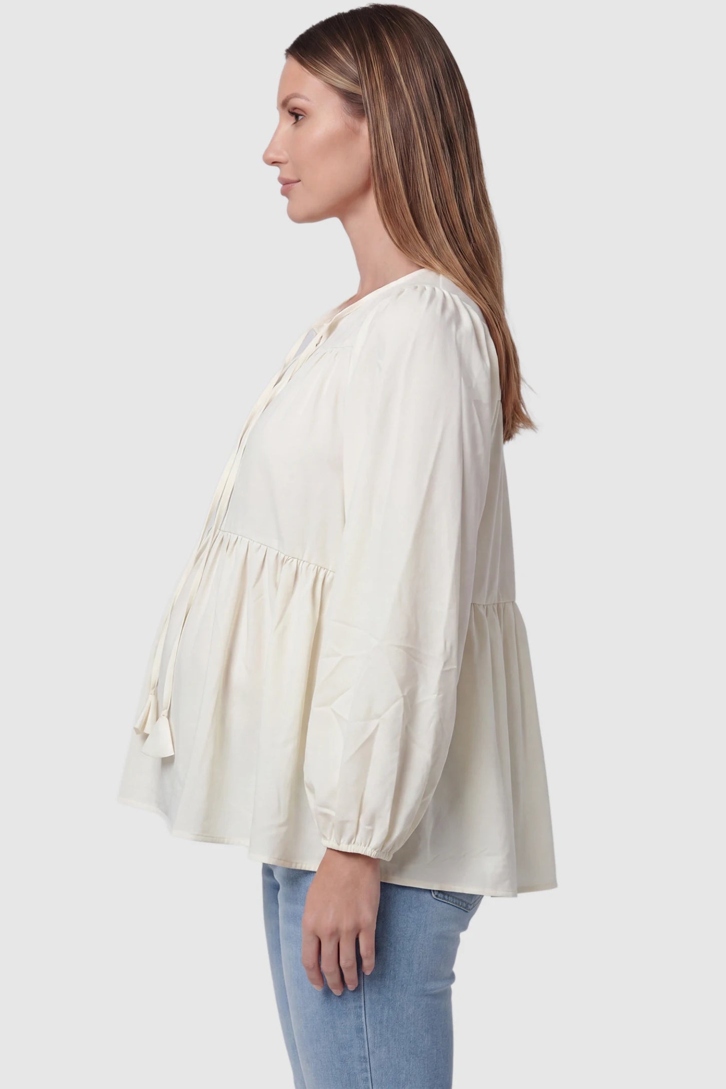 Tie-front tassel long sleeve peplum maternity blouse in pale yellow with bump-friendly relaxed fit, side view on pregnant model