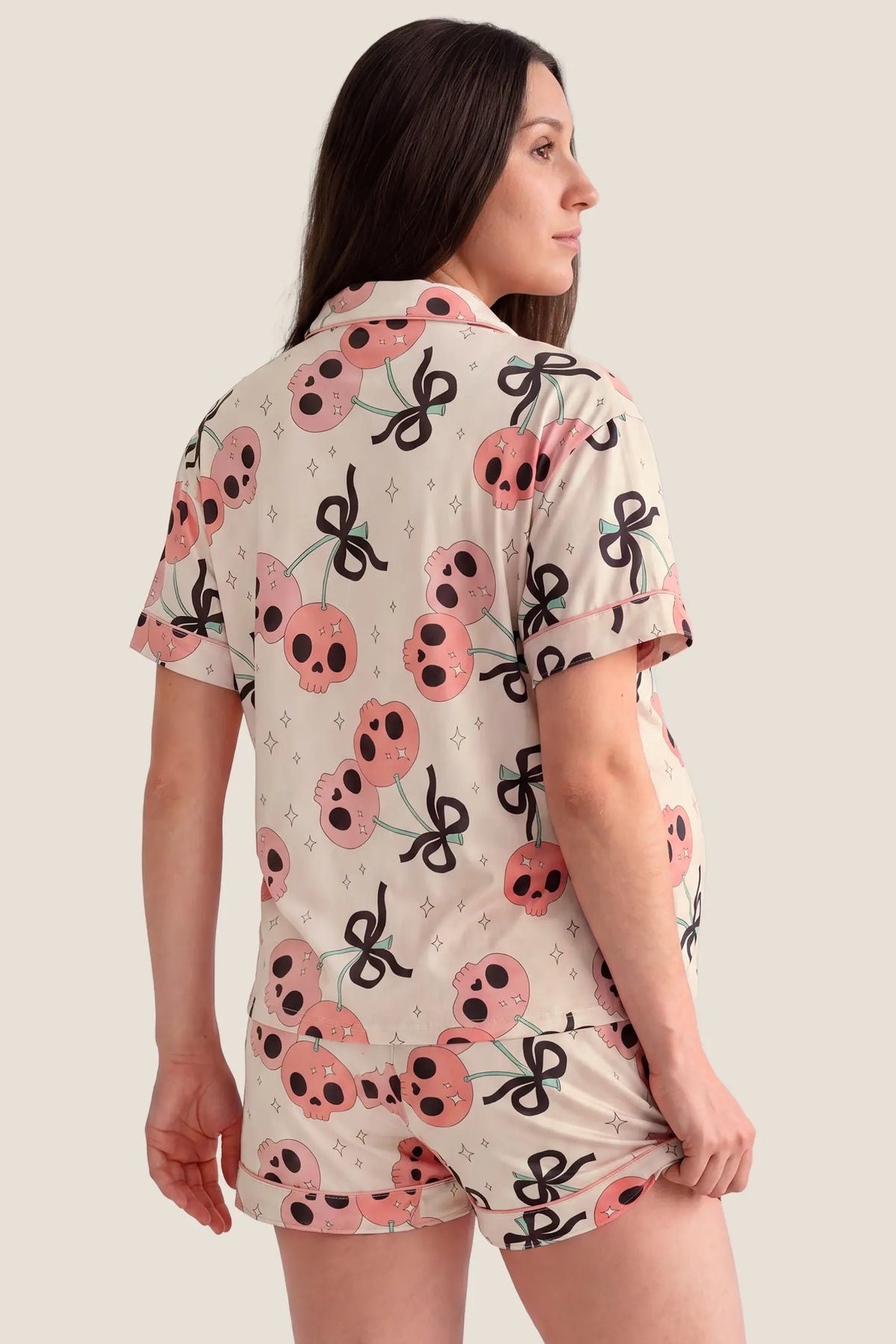 Pink Skull Cherry Button-Up Maternity Pajama Set Pink Skull Cherry Button-Up Maternity Pajama Set in Pink Skull featuring full back coverage, lightweight Halloween print fabric, short sleeves, and matching shorts on a pregnant model, back view.
