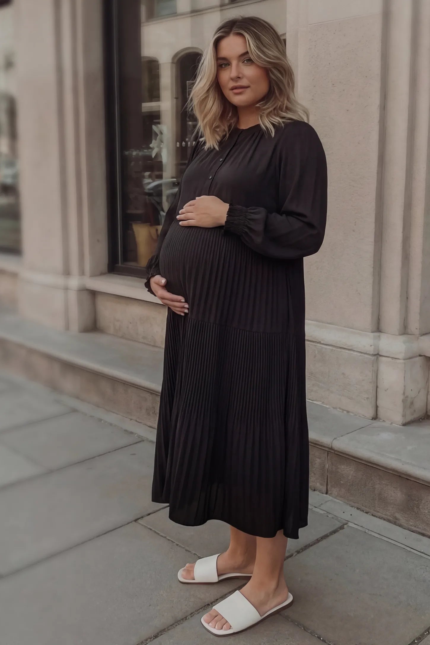 Button-up neck pleated tiered maternity midi dress in black with soft pleated design, side view on pregnant model