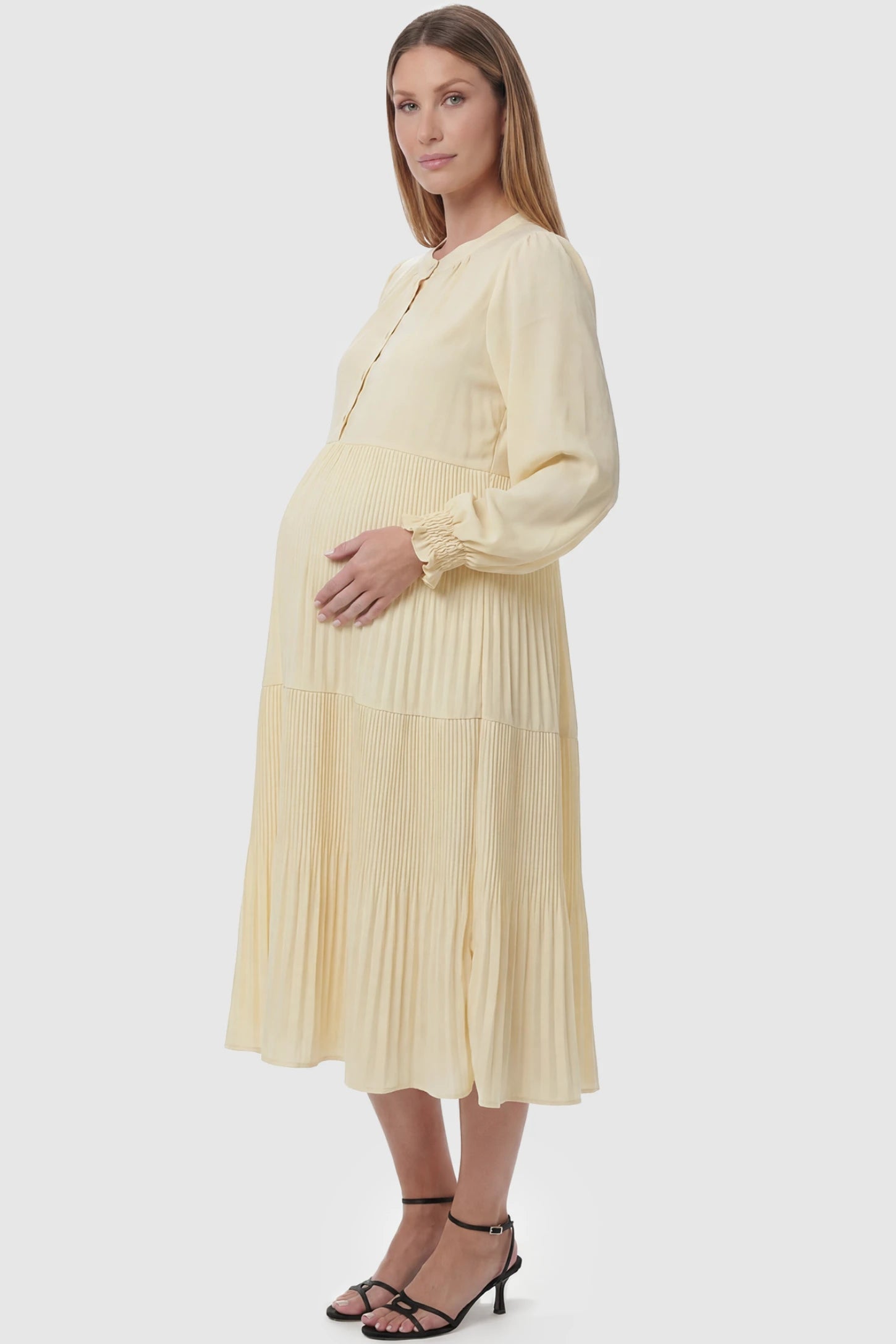 Button-Up Neck Pleated Tiered Maternity Midi Dress Button-up neck pleated tiered maternity midi dress in pale yellow with soft pleated design, side view on pregnant model