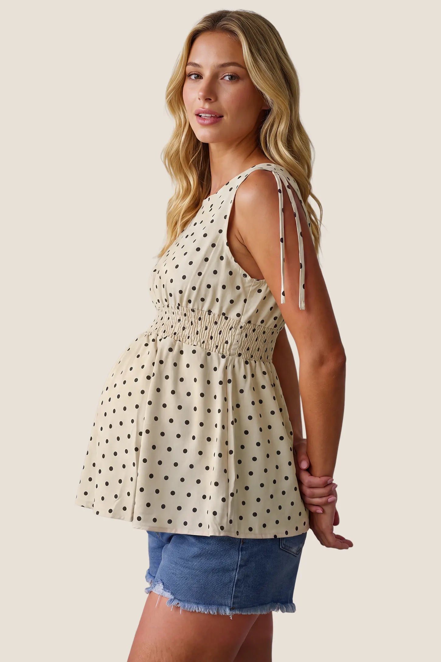 Polka Dot Round Neck Flowy Maternity Top in Beige featuring a flowy fit, elasticated waistband, lightweight stretch fabric, and a comfortable maternity-friendly silhouette on a pregnant model, side view.