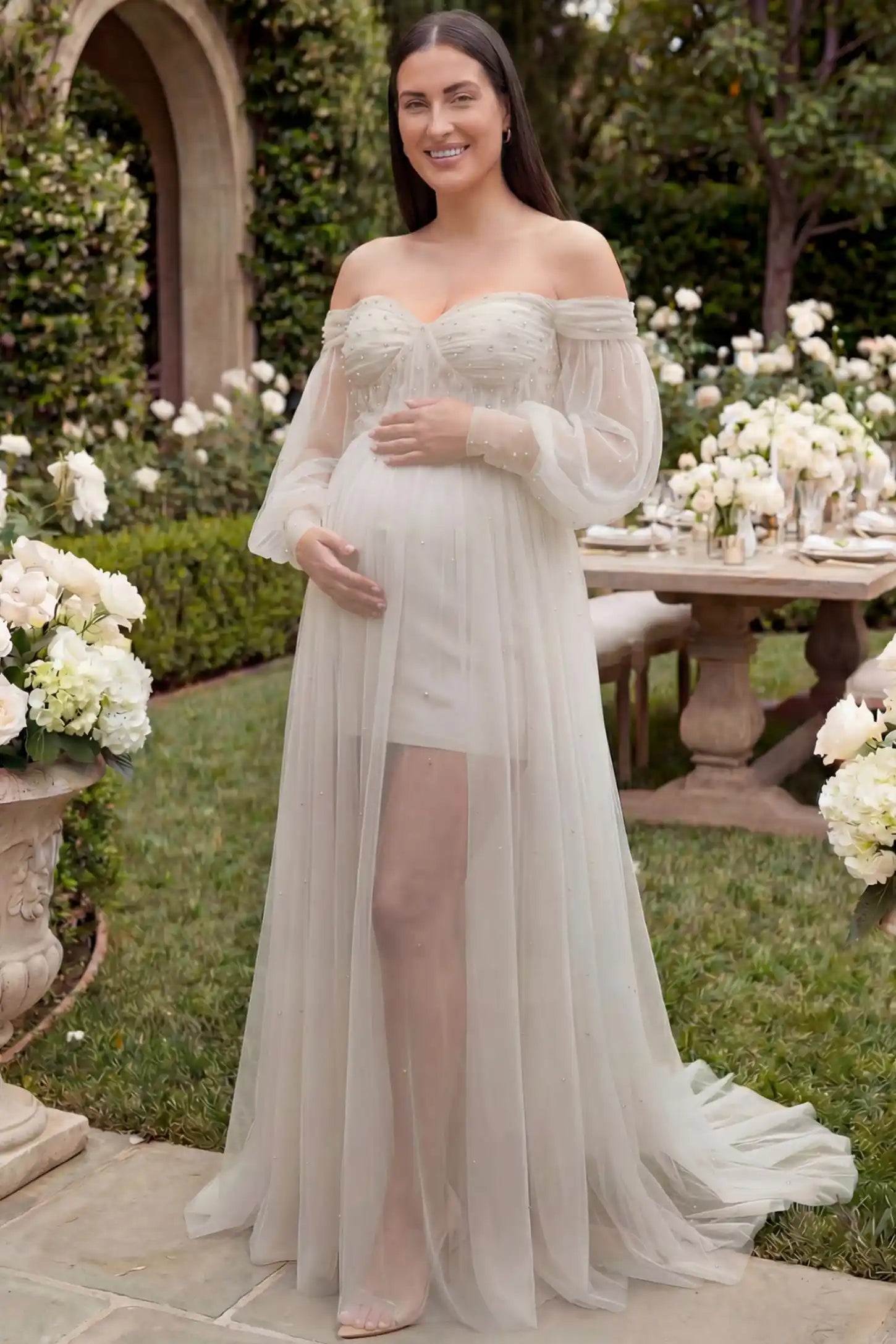 Off-Shoulder Empire Waist Maternity Gown Off-Shoulder Empire Waist Maternity Gown in ivory featuring a sweetheart neckline and flowy A-line silhouette on a plus size pregnant model, front view.