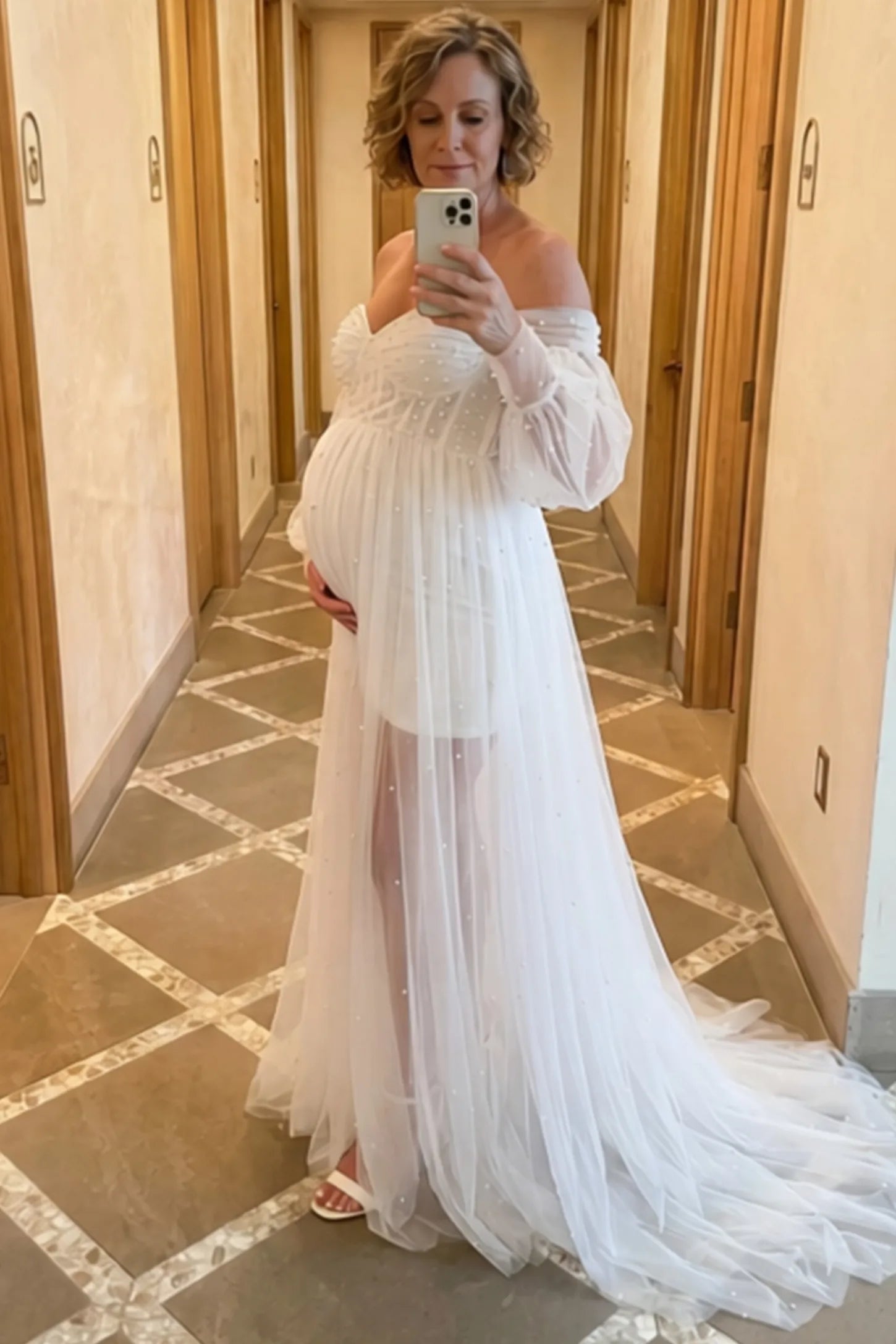 Off-Shoulder Empire Waist Maternity Gown Off-Shoulder Empire Waist Maternity Gown in white featuring a sweetheart neckline and flowy A-line silhouette on a pregnant woman, front view.