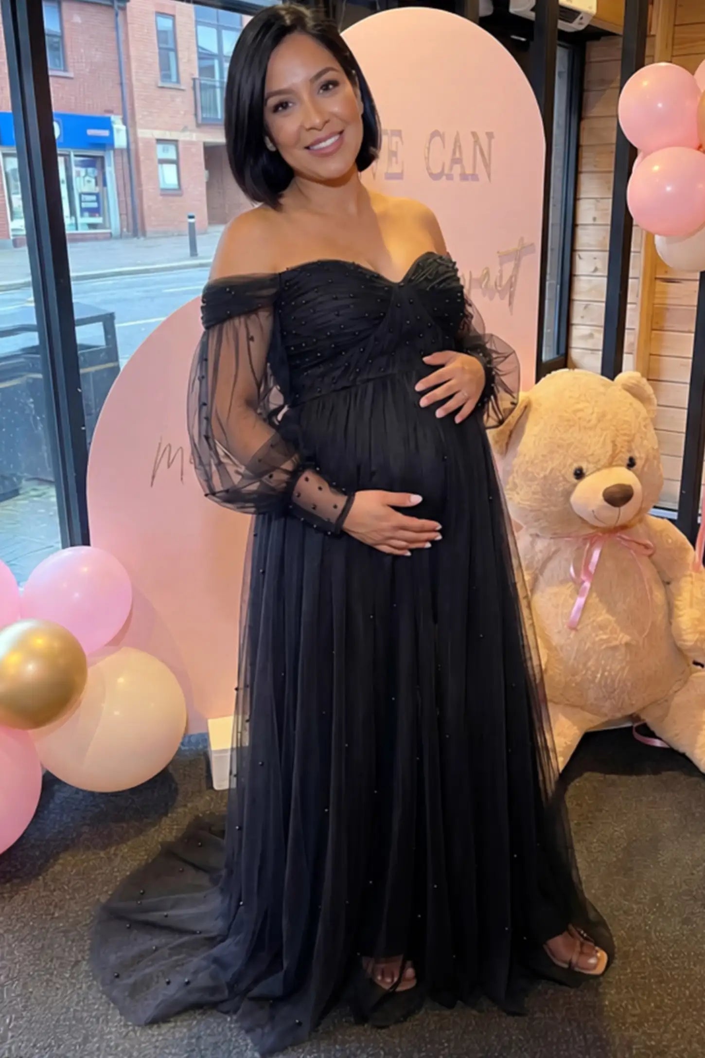 Off-Shoulder Empire Waist Maternity Gown Off-Shoulder Empire Waist Maternity Gown in black featuring a sweetheart neckline and flowy A-line silhouette on a pregnant woman, front view.