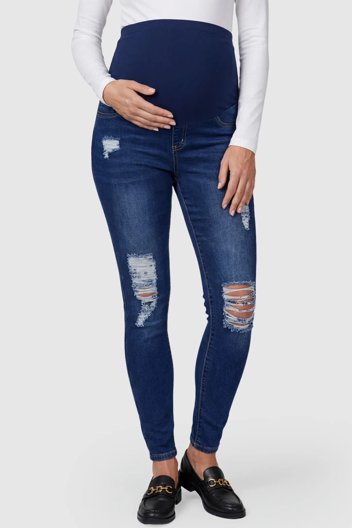 Distressed ripped high-waist skinny maternity jeans in dark blue with ripped design, front view on pregnant model