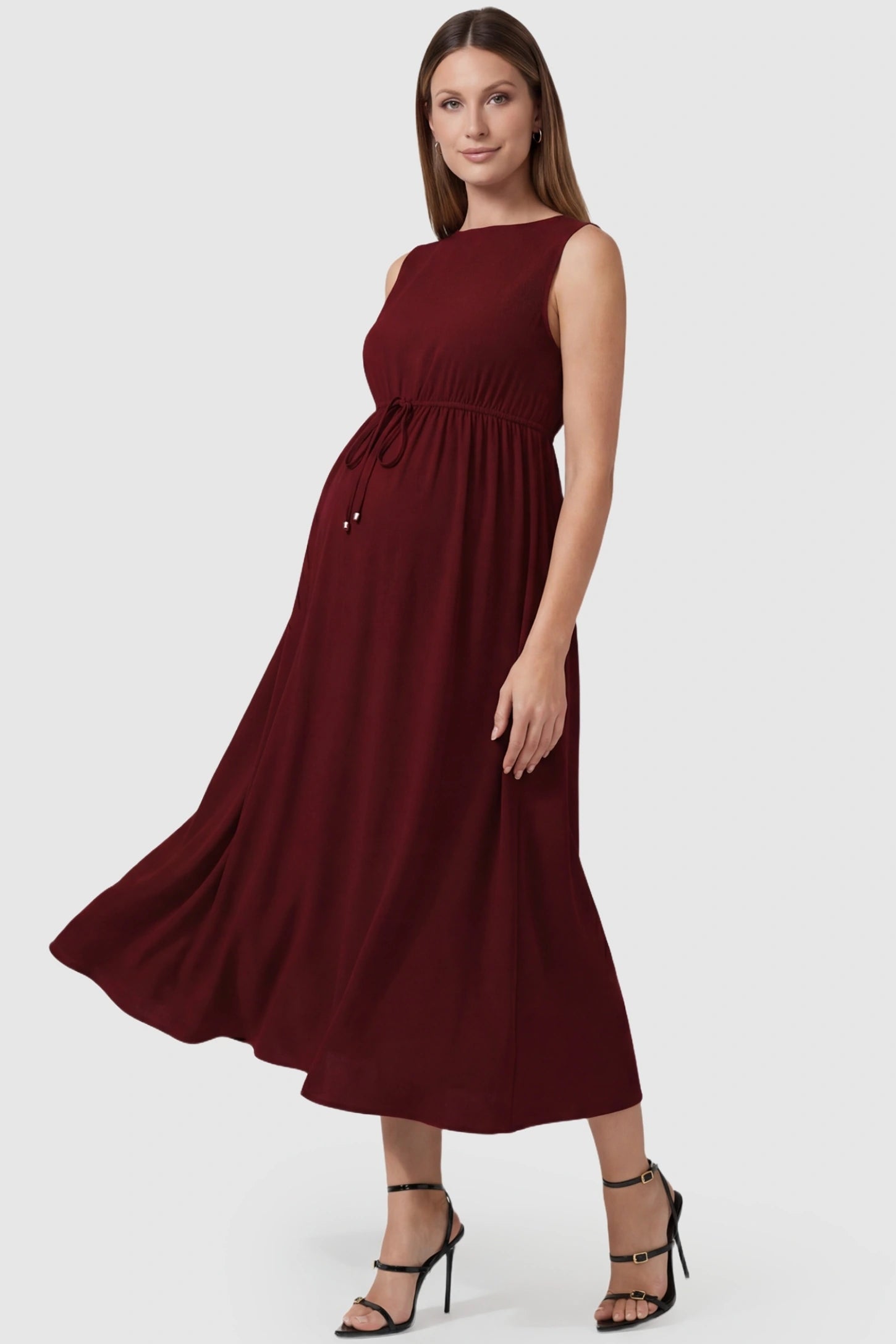Drawstring Waist Sleeveless Full Skirt Maternity Skater Dress Drawstring Waist Sleeveless Maternity Skater Dress in Burgundy featuring a side profile bump view on a pregnant model.