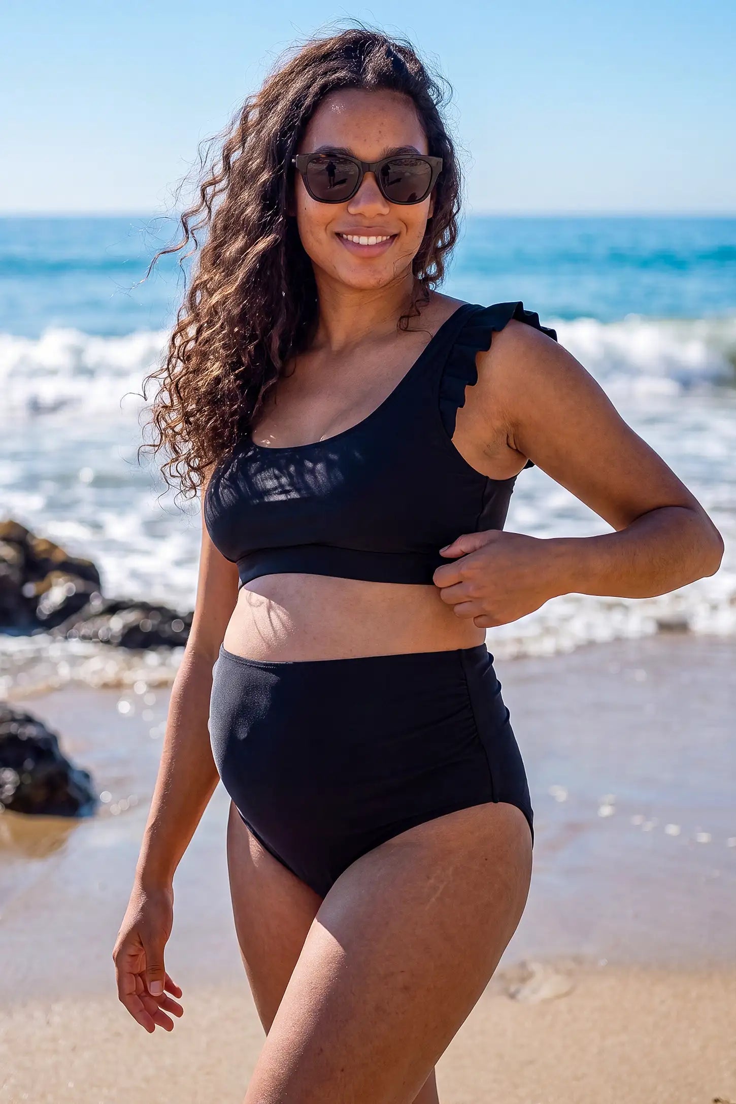 Ruffle Strap High Waisted Two-Piece Bikini Ruffle Strap High Waisted Two-Piece Bikini in Black featuring ruffle shoulder straps, a supportive bikini top, matching high-waisted bottoms, and a flattering maternity-friendly fit on a pregnant model, front view.