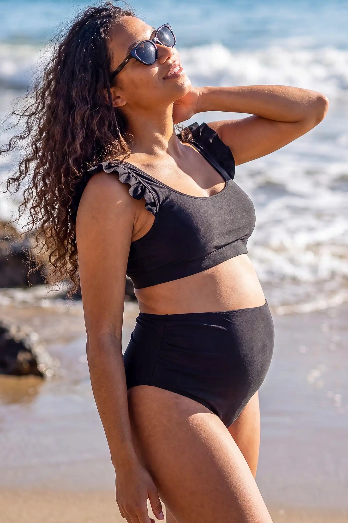 Ruffle Strap High Waisted Two-Piece Bikini Ruffle Strap High Waisted Two-Piece Bikini in Black featuring feminine ruffle straps, a sleek two-piece silhouette, and high-waisted bottoms on a pregnant model, side view.