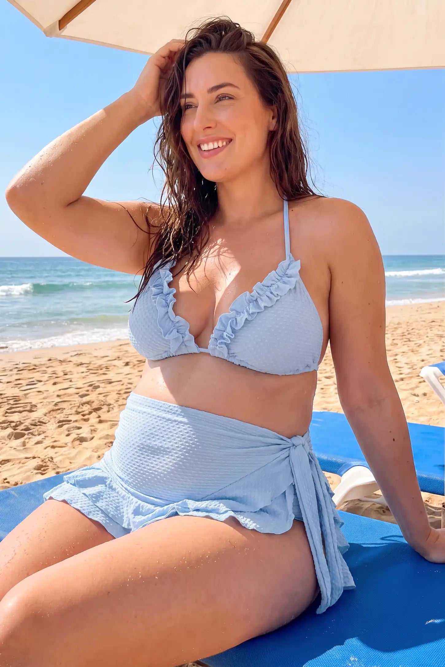 Ruffled Trim Halter Maternity Bikini Set Ruffled Trim Halter Maternity Bikini Set in Blue featuring a halter neckline, open back design, high-waist bikini bottom, side ruched panels, and matching ruffled sarong cover-up on a plus size pregnant model, front view.