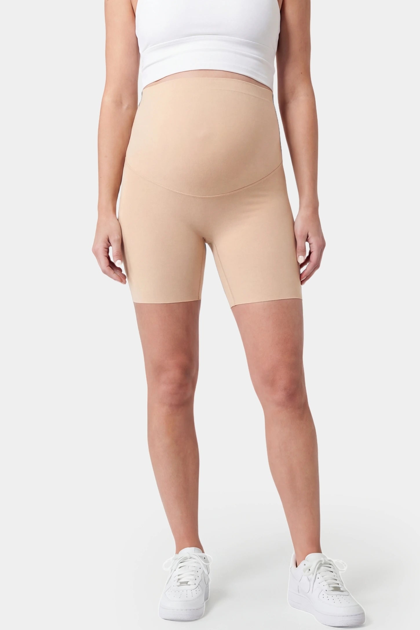 Seamless Belly Support Mid-Thigh Shaping Maternity Shorts Seamless belly support mid-thigh shaping maternity shorts in beige with high-waist support, front view on pregnant model