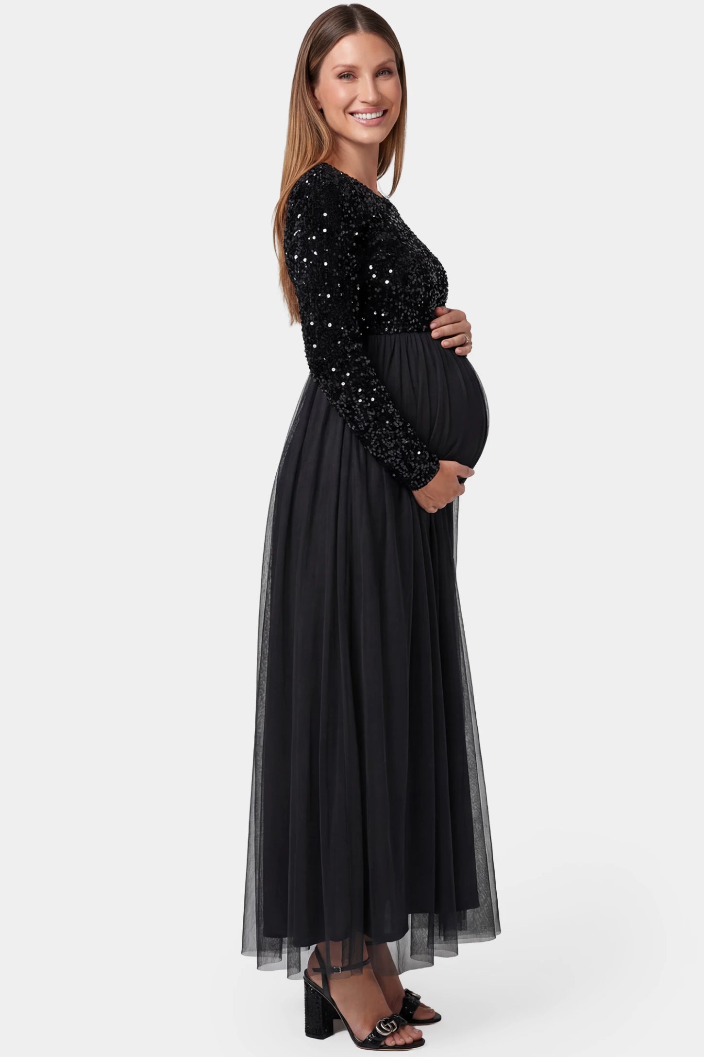 Sequined Mesh Long-Sleeve Maxi Maternity Gown Sequined mesh long sleeve maxi maternity gown in black featuring flowing mesh skirt in full body side view on a pregnant model