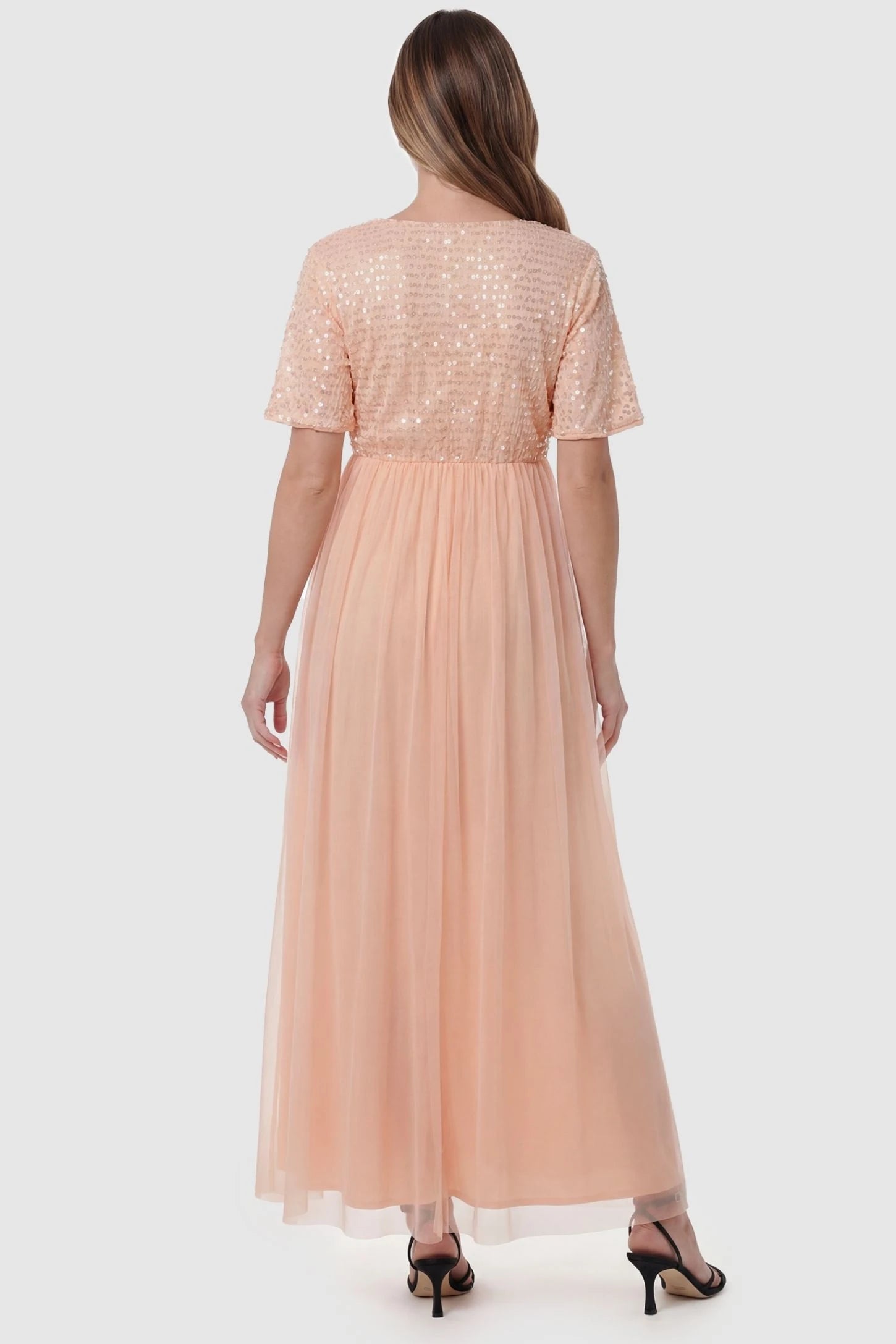 Sequin Ruffle Sleeve Maternity Dress Sequin Ruffle Sleeve Maternity Photoshoot Dress in Pink featuring a flowy tulle skirt on a pregnant model, back view.