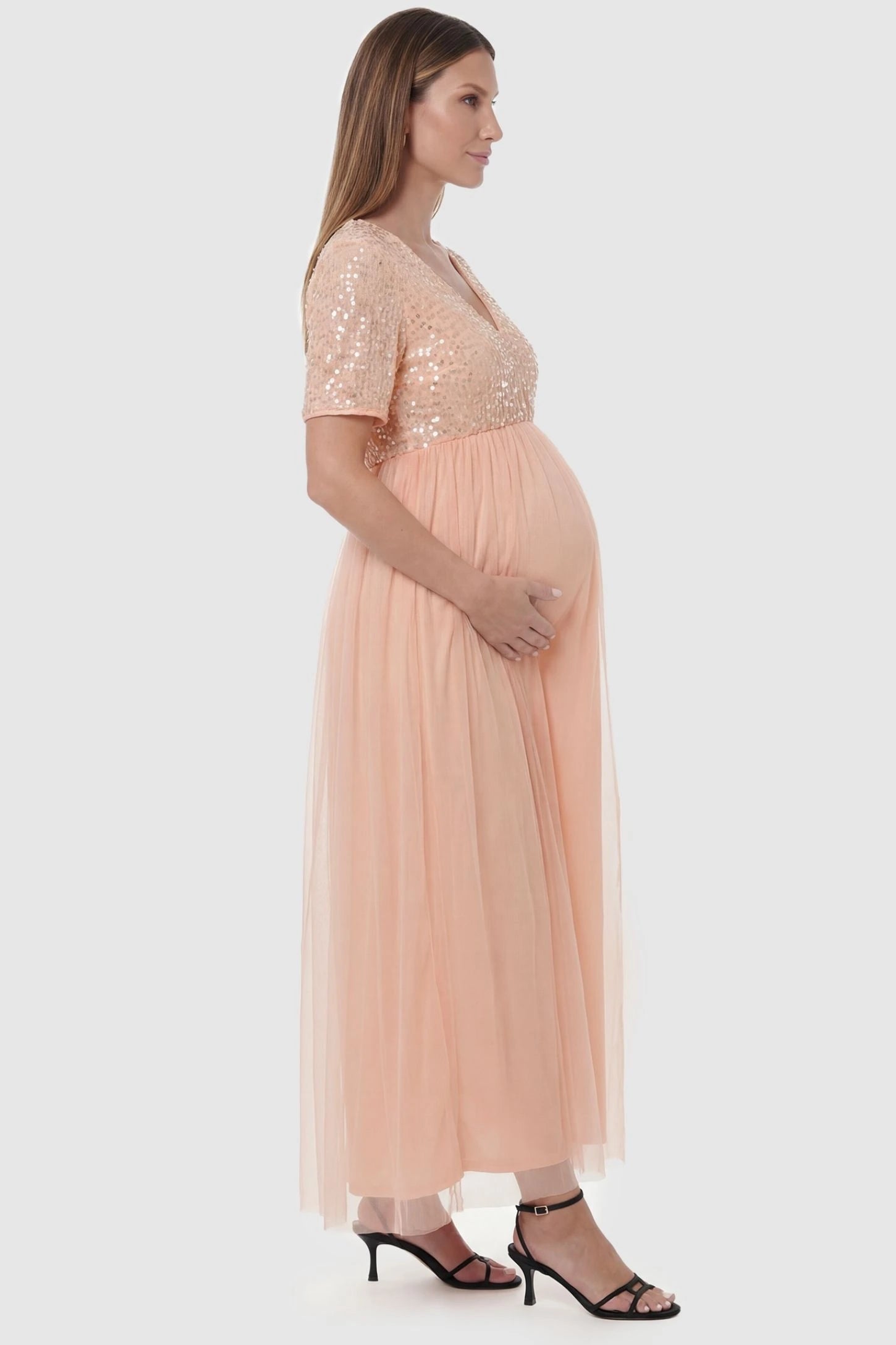 Sequin Ruffle Sleeve Maternity Dress Sequin Ruffle Sleeve Maternity Photoshoot Dress in Pink featuring a flowy tulle skirt on a pregnant model, side view.