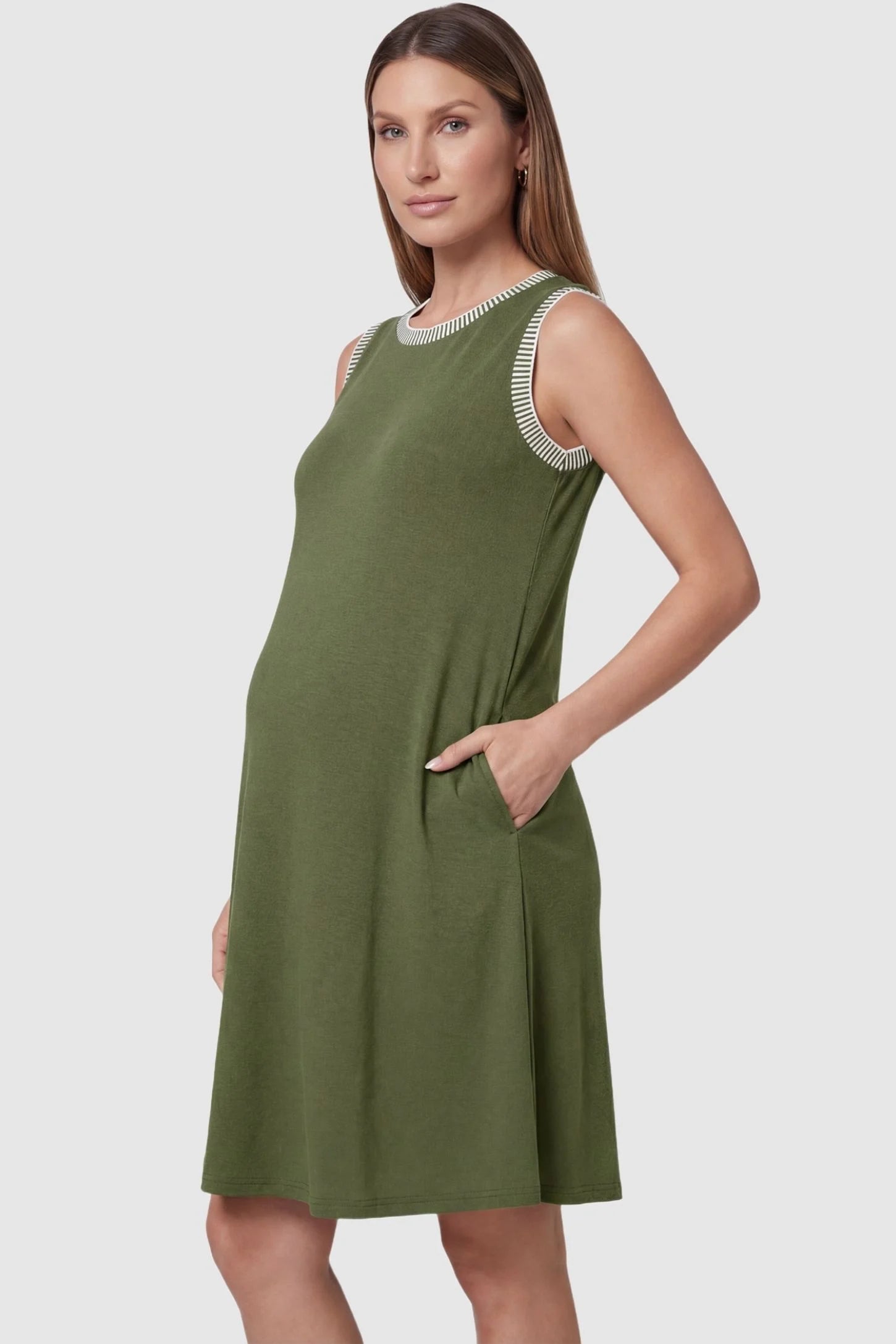 Sleeveless round neck A-line short maternity dress in army green featuring functional side pockets in side view on a pregnant model