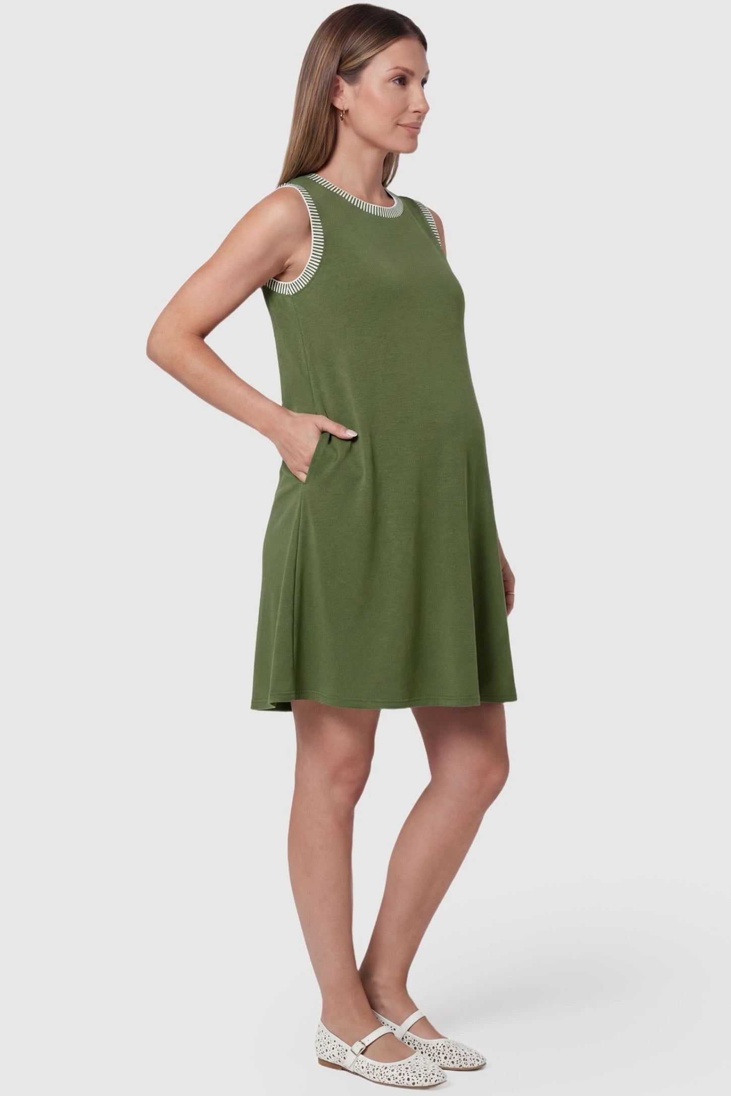 Sleeveless round neck A-line short maternity dress in army green featuring functional side pockets in side view on a pregnant model