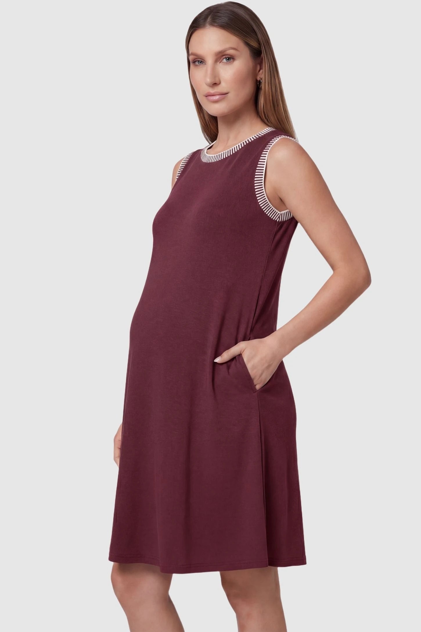 Sleeveless Round Neck A-Line Short Maternity Dress Sleeveless round neck A-line short maternity dress in burgundy featuring functional side pockets in side view on a pregnant model