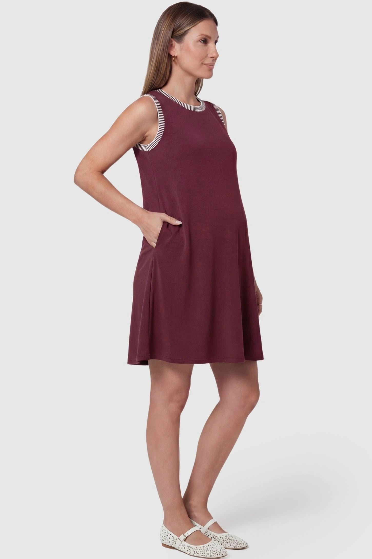 Sleeveless Round Neck A-Line Short Maternity Dress Sleeveless round neck A-line short maternity dress in burgundy featuring functional side pockets in side view on a pregnant model